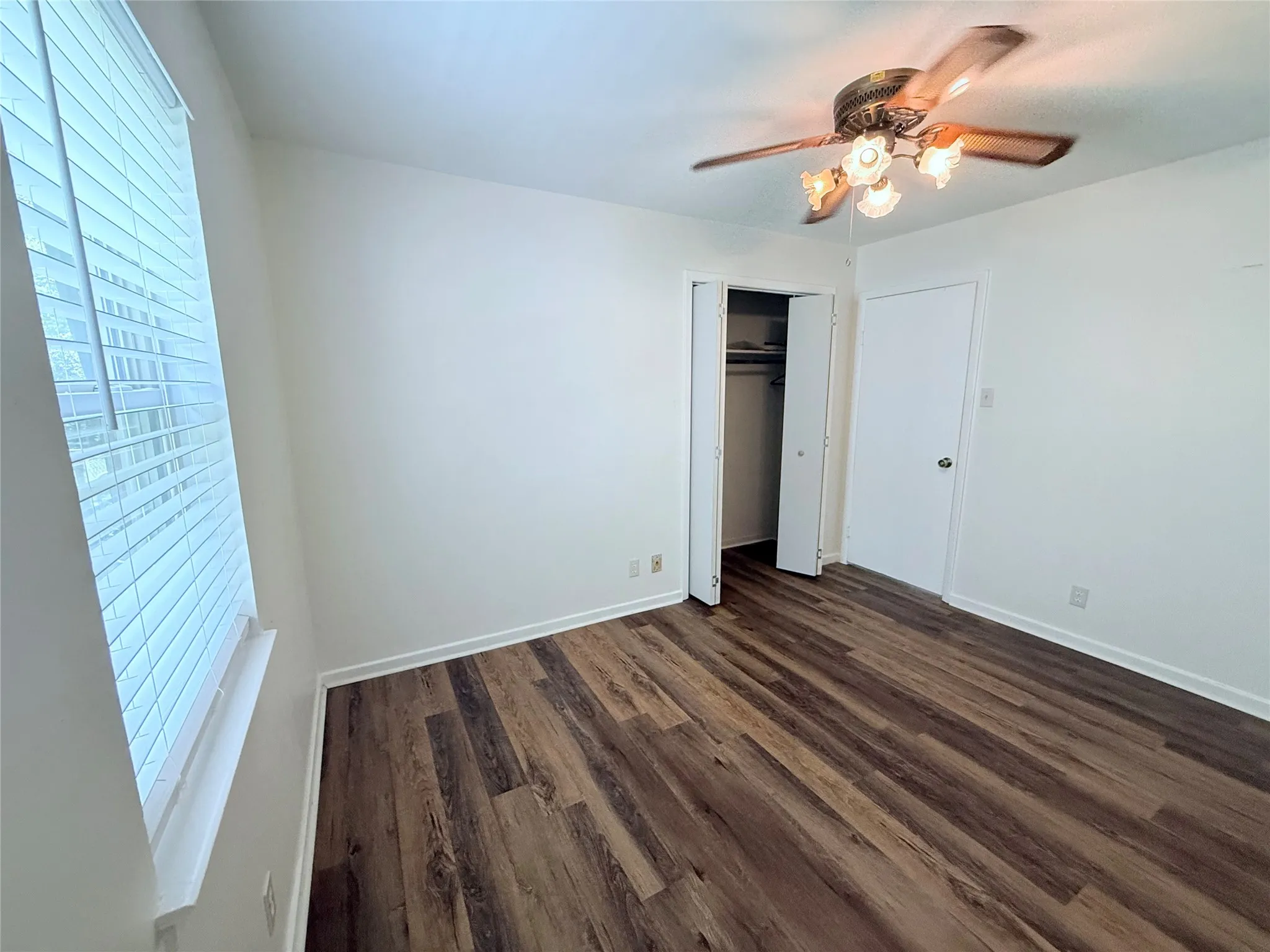Room featuring wood-finish flooring, a window with blinds, a ceiling fan with integrated lighting, and a closet with bifold doors