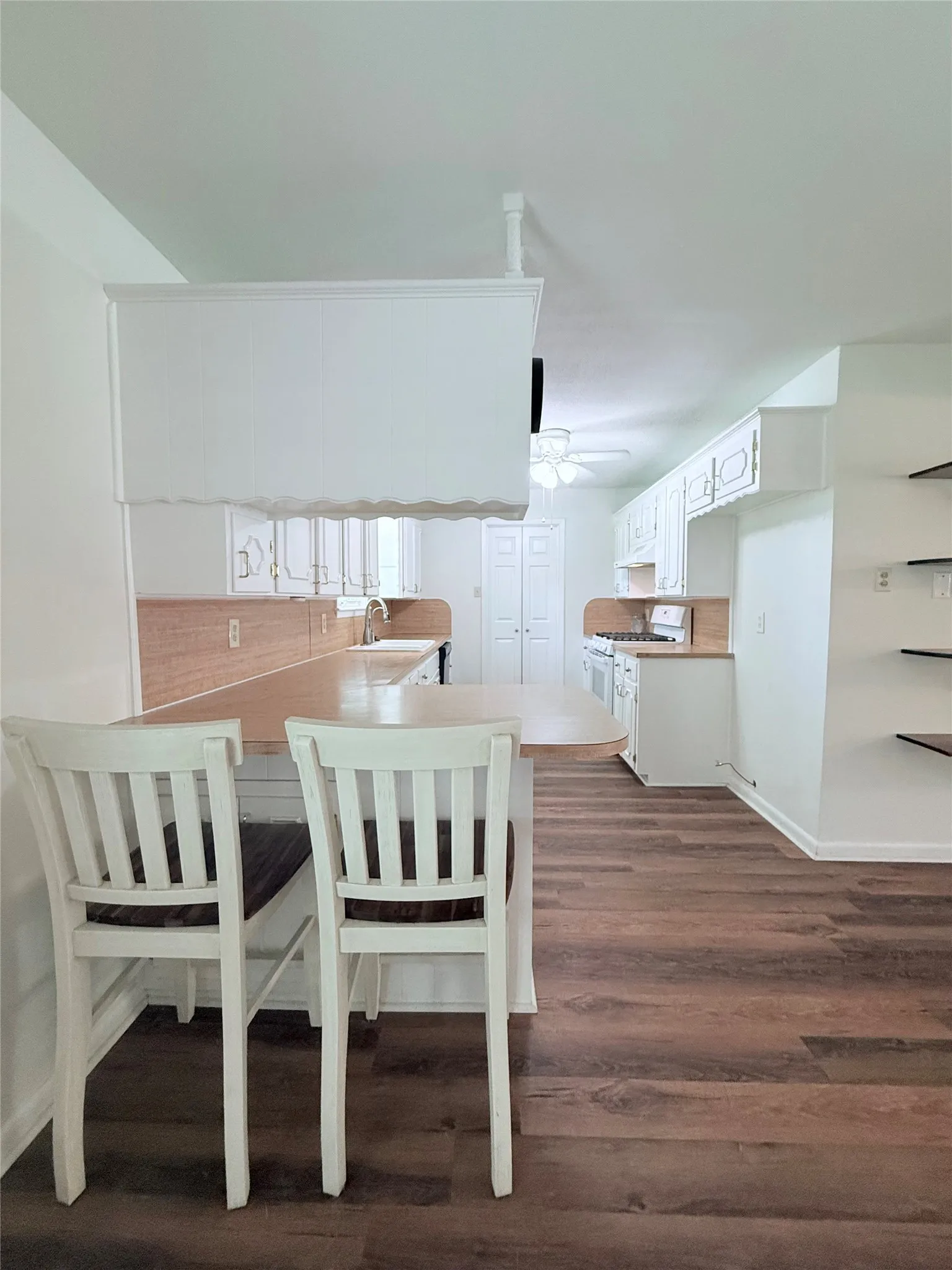 Open-concept kitchen featuring wood-finish flooring, white cabinetry, and a peninsula with countertop seating