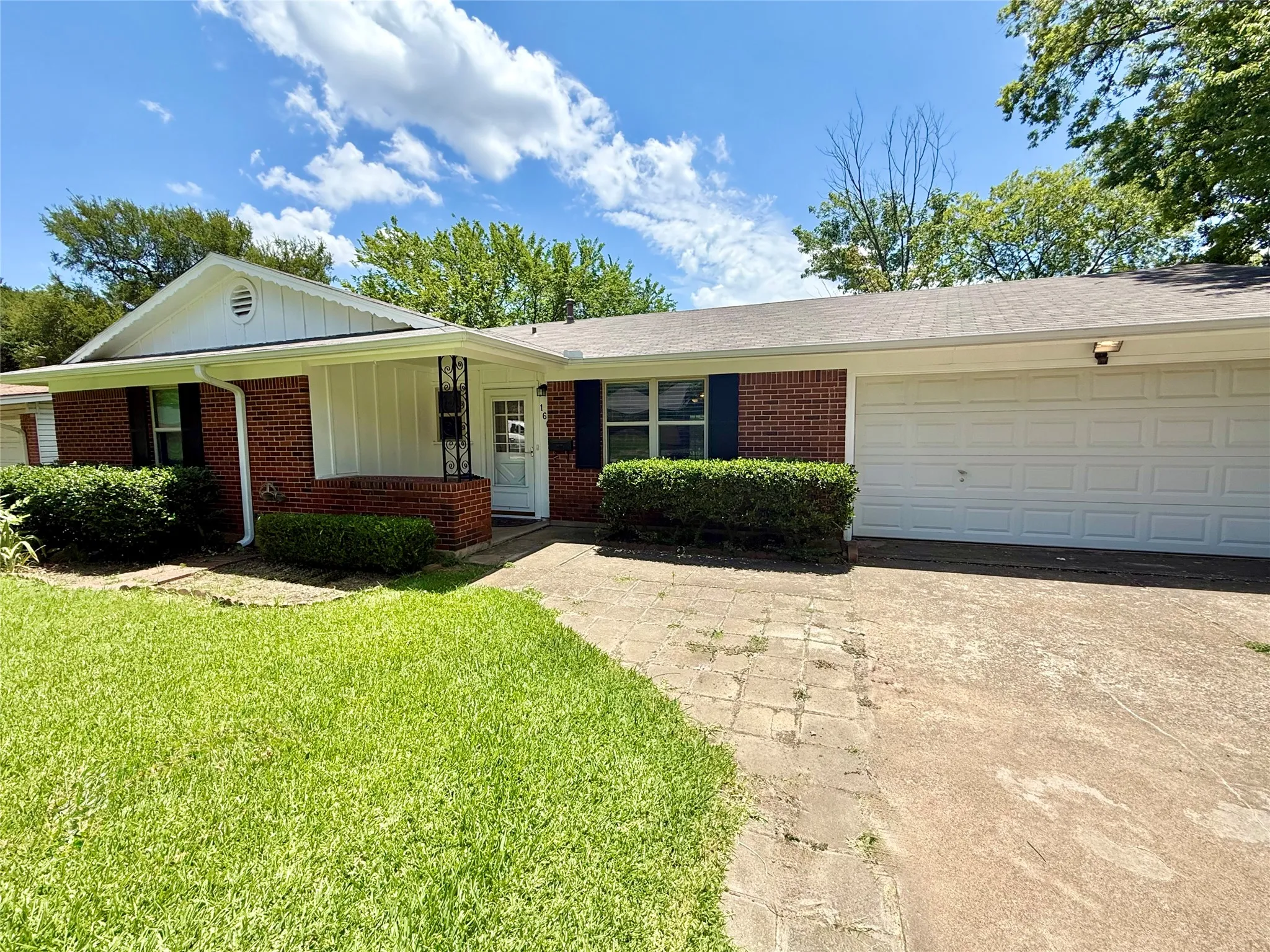 Brick exterior with white trim, featuring a two-car garage, mature landscaping, and an inviting front entrance