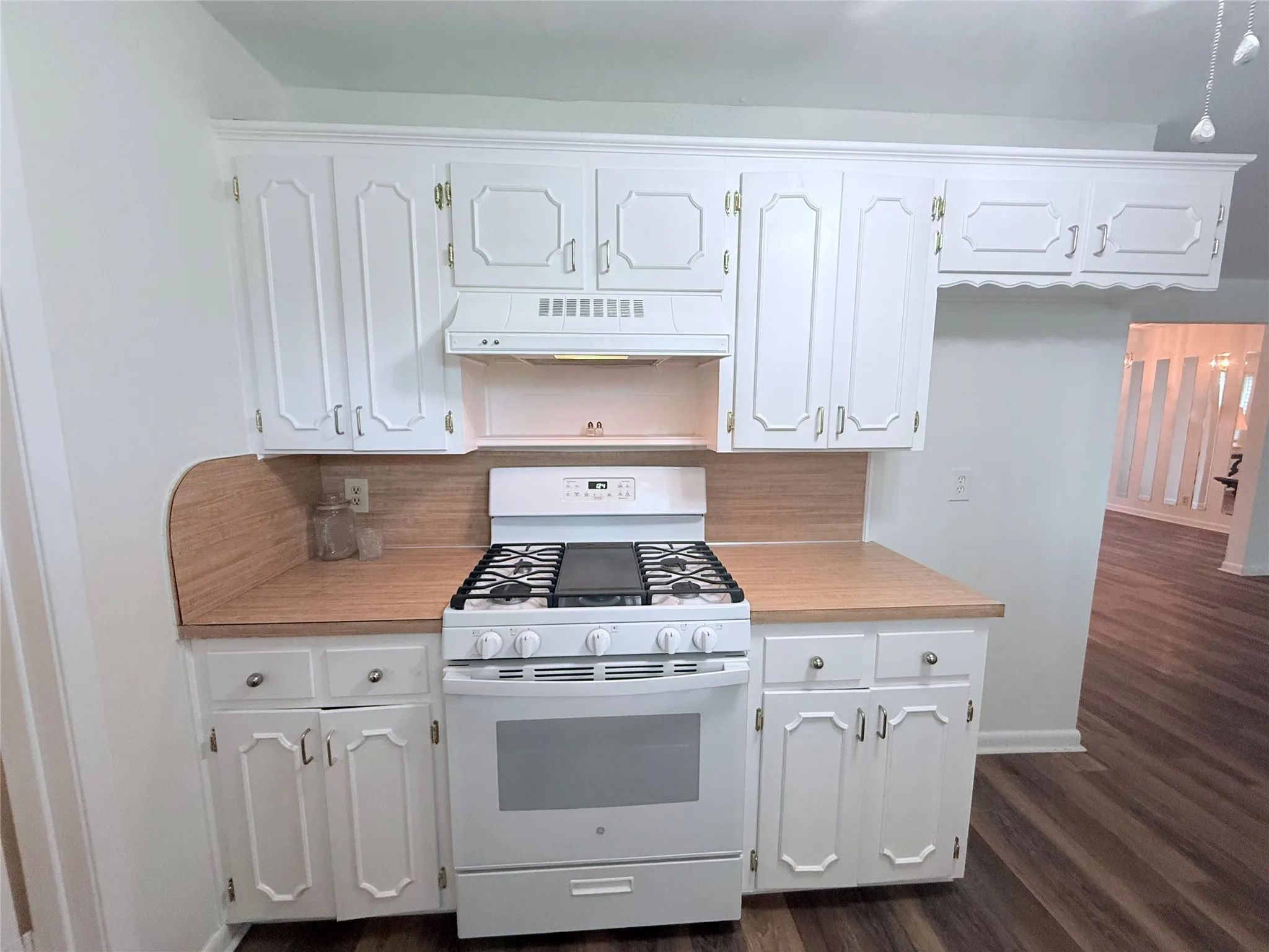 Kitchen featuring white cabinetry with decorative paneling and gold-tone hardware, a white gas range with a griddle, wood-finish countertops, and matching wood-finish backsplash