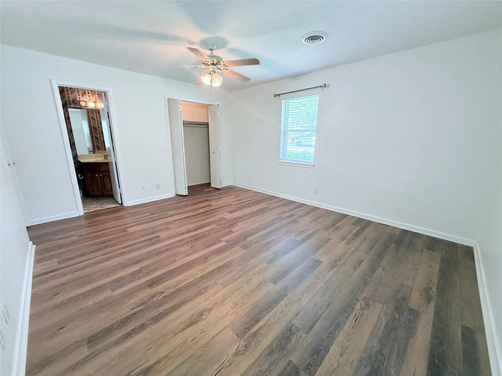 Spacious room featuring wood-finish flooring, a ceiling fan with integrated lighting, a window with blinds, and a built-in closet with bi-fold doors