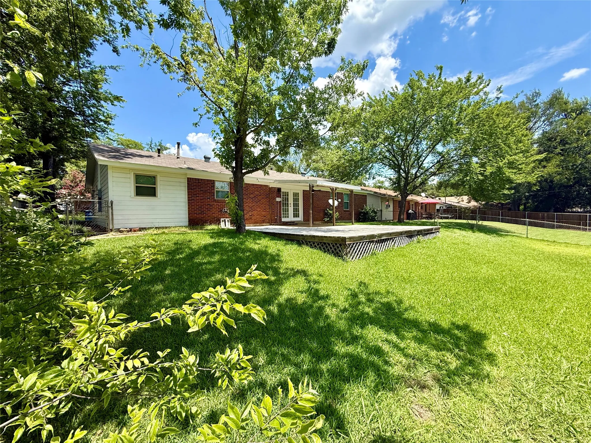 Expansive backyard featuring a large wooden deck, mature trees, a red brick exterior, and white siding