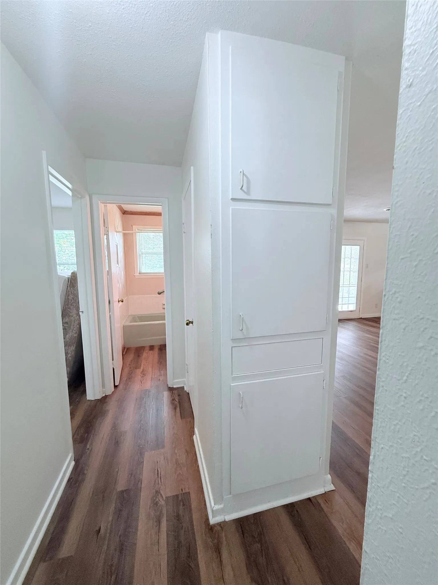 Hallway featuring wood-finish flooring, white walls, and built-in white cabinetry providing vertical storage