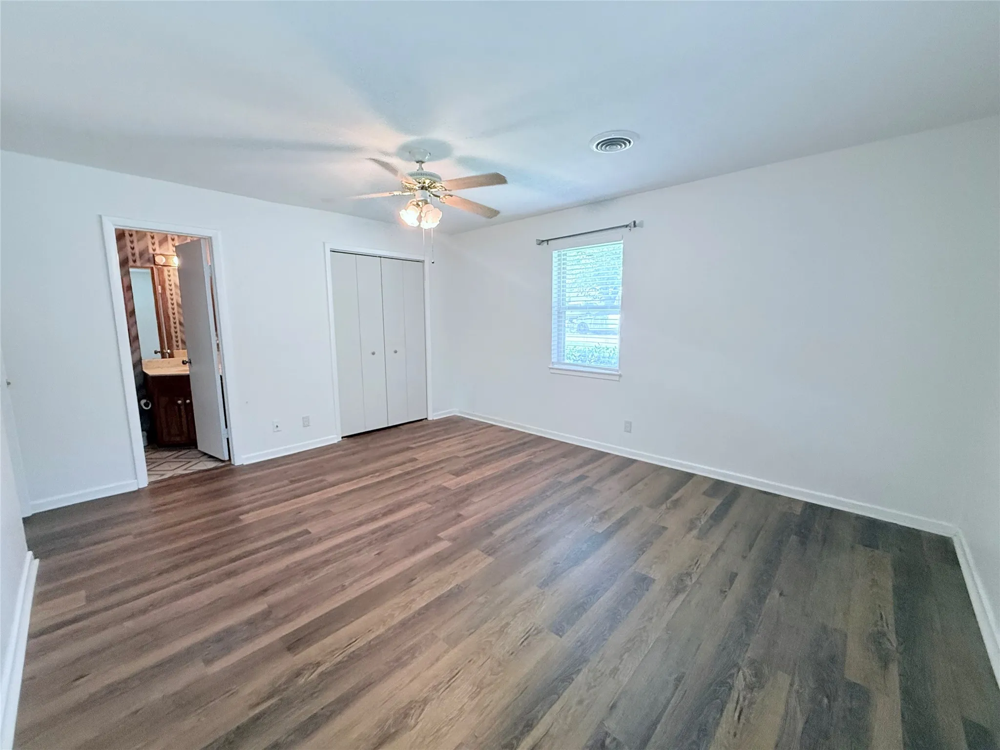 Room featuring wood-finish flooring, a ceiling fan with integrated lighting, a window with blinds, and bi-fold closet doors