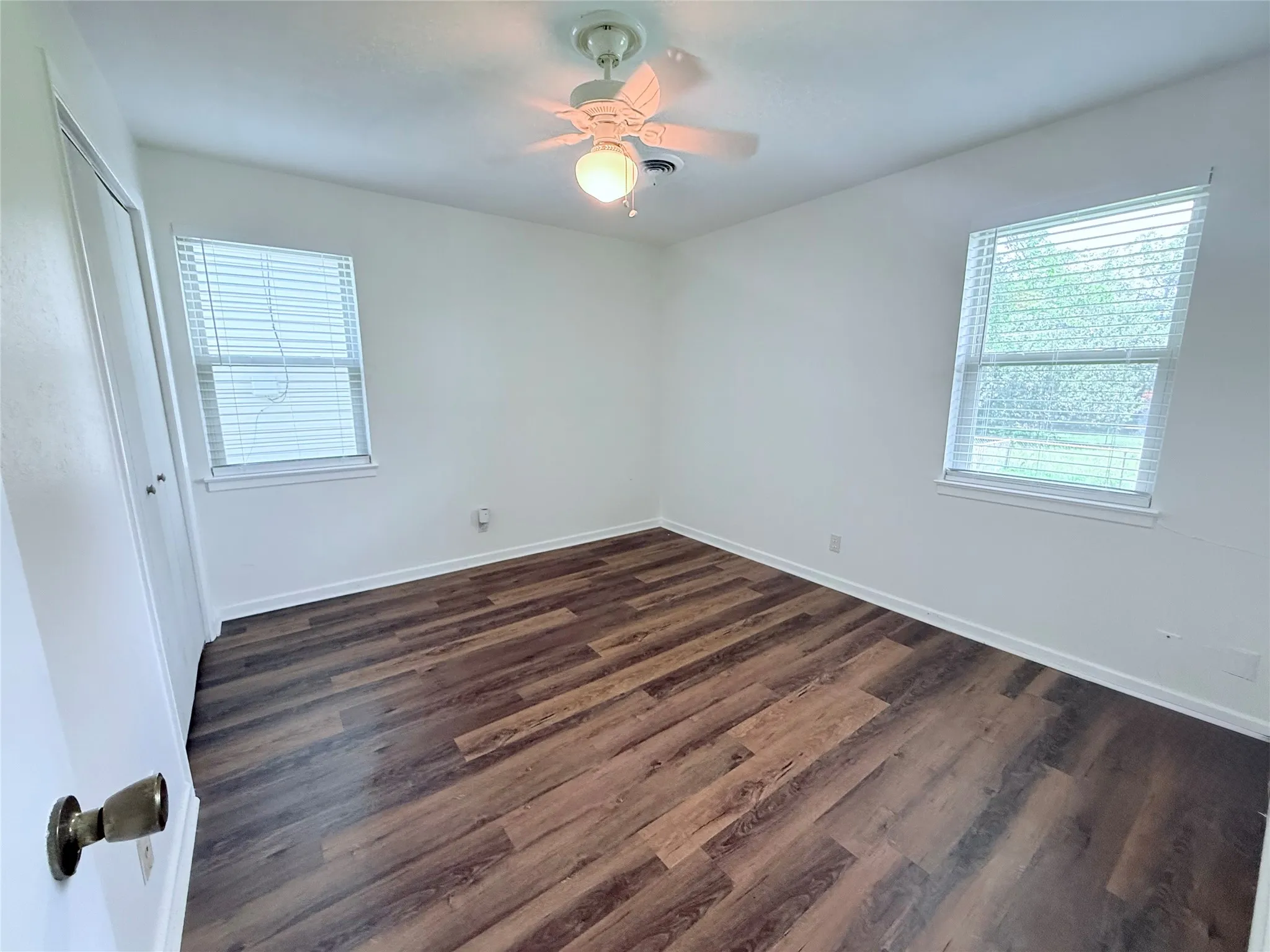 Spacious room featuring wood-finish flooring, white baseboards, and two windows with blinds