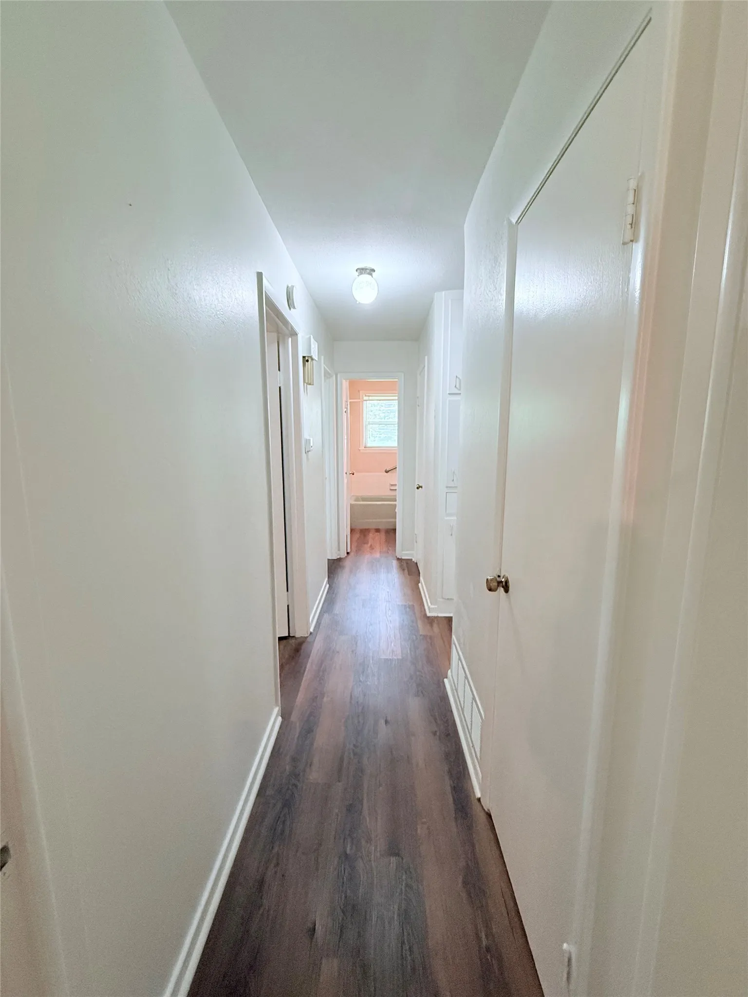 Corridor featuring wood-finish flooring, light-toned walls, and flush-mount lighting