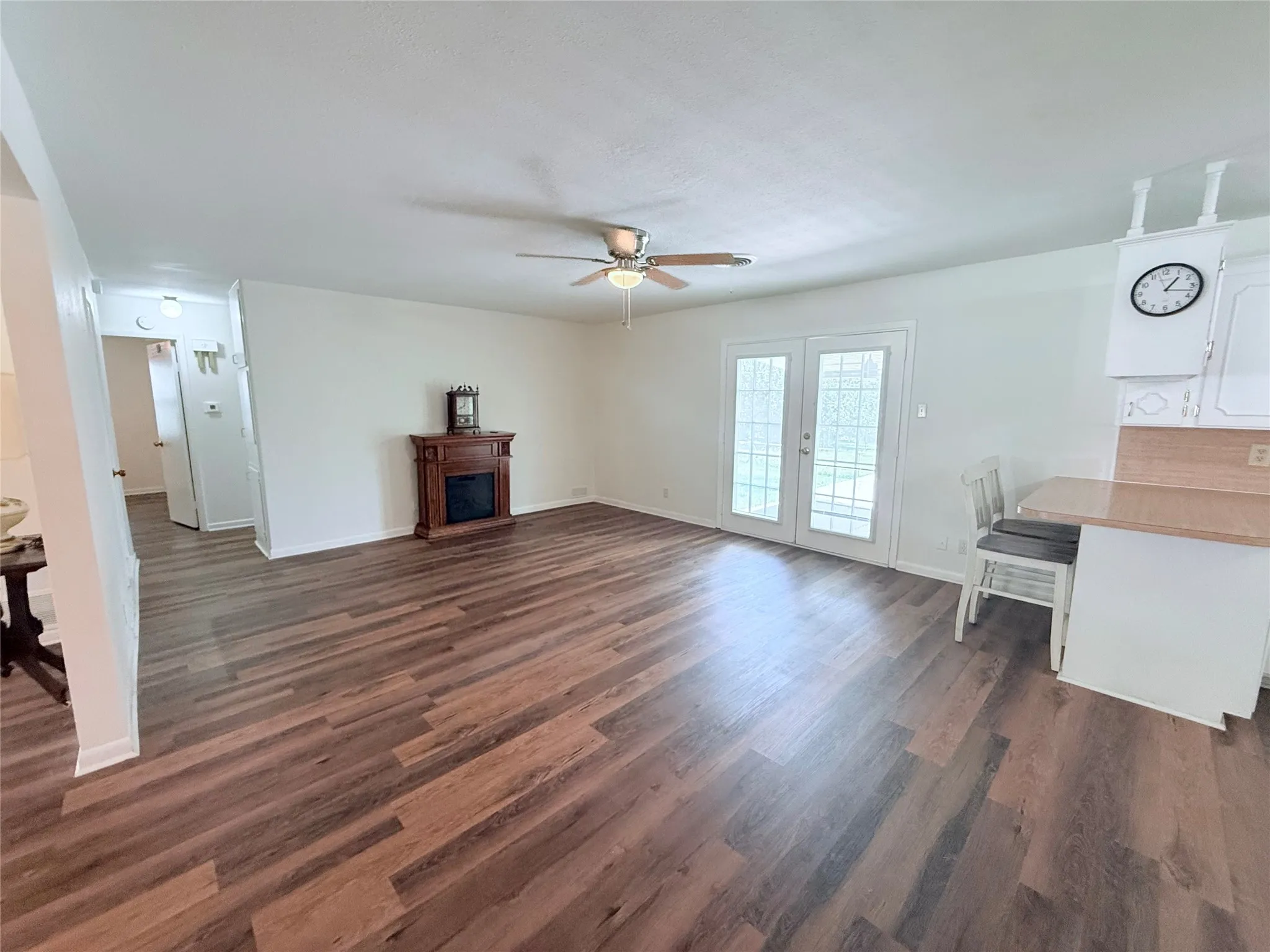 Expansive room featuring wood-finish flooring, a built-in fireplace mantel, and ceiling fan