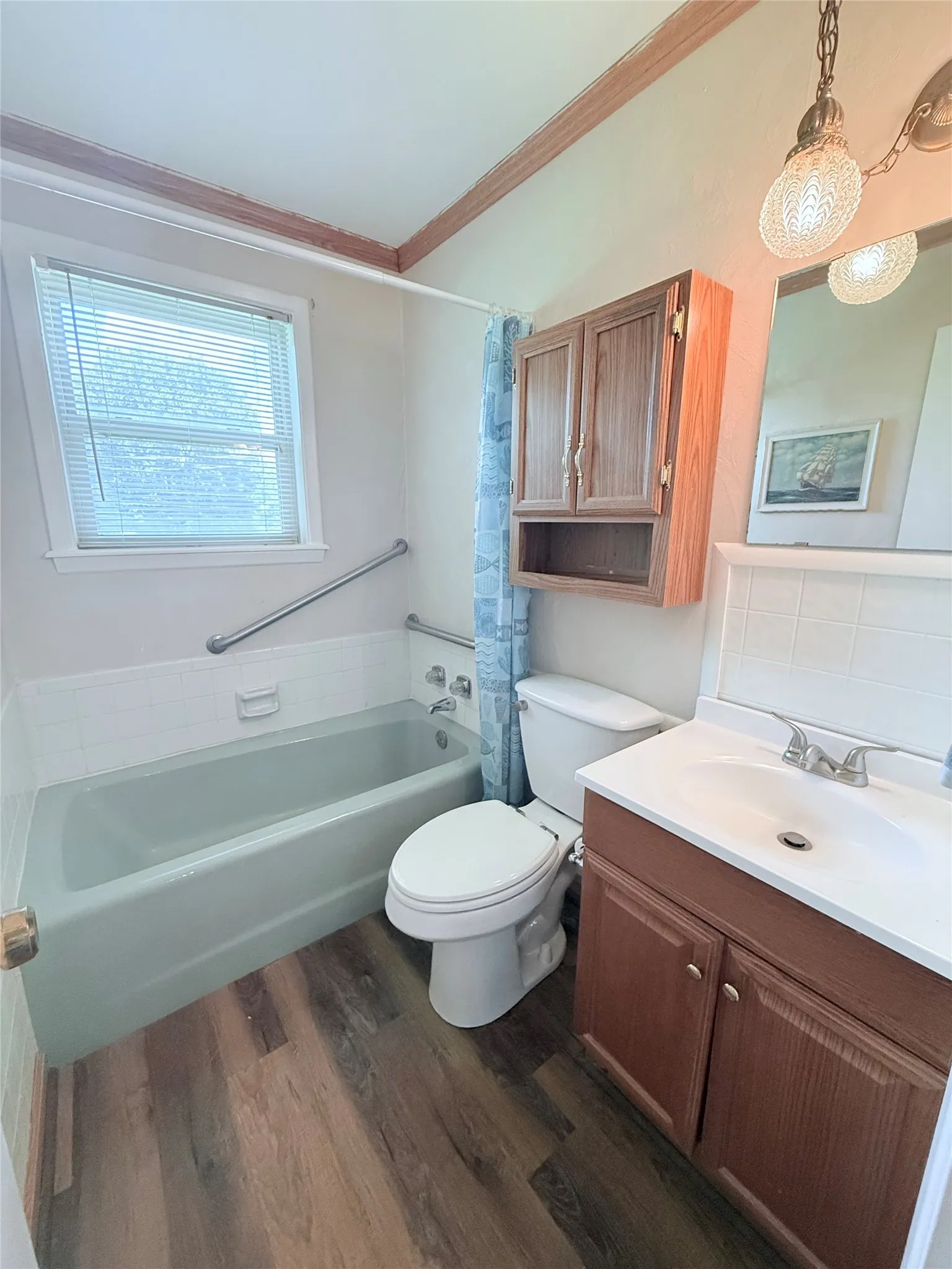 Bathroom featuring a bathtub with a grab bar, wood-finish flooring, a wood vanity with integrated sink, a wall-mounted wooden cabinet, and a window with blinds