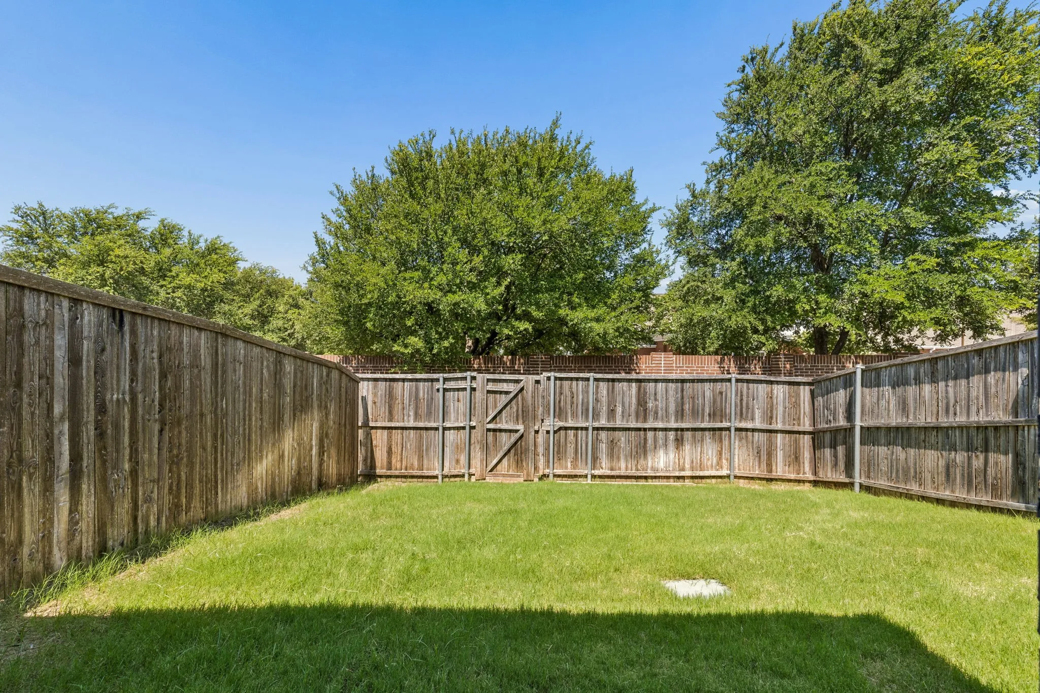 Expansive backyard featuring a manicured lawn, full privacy fencing, and mature perimeter trees