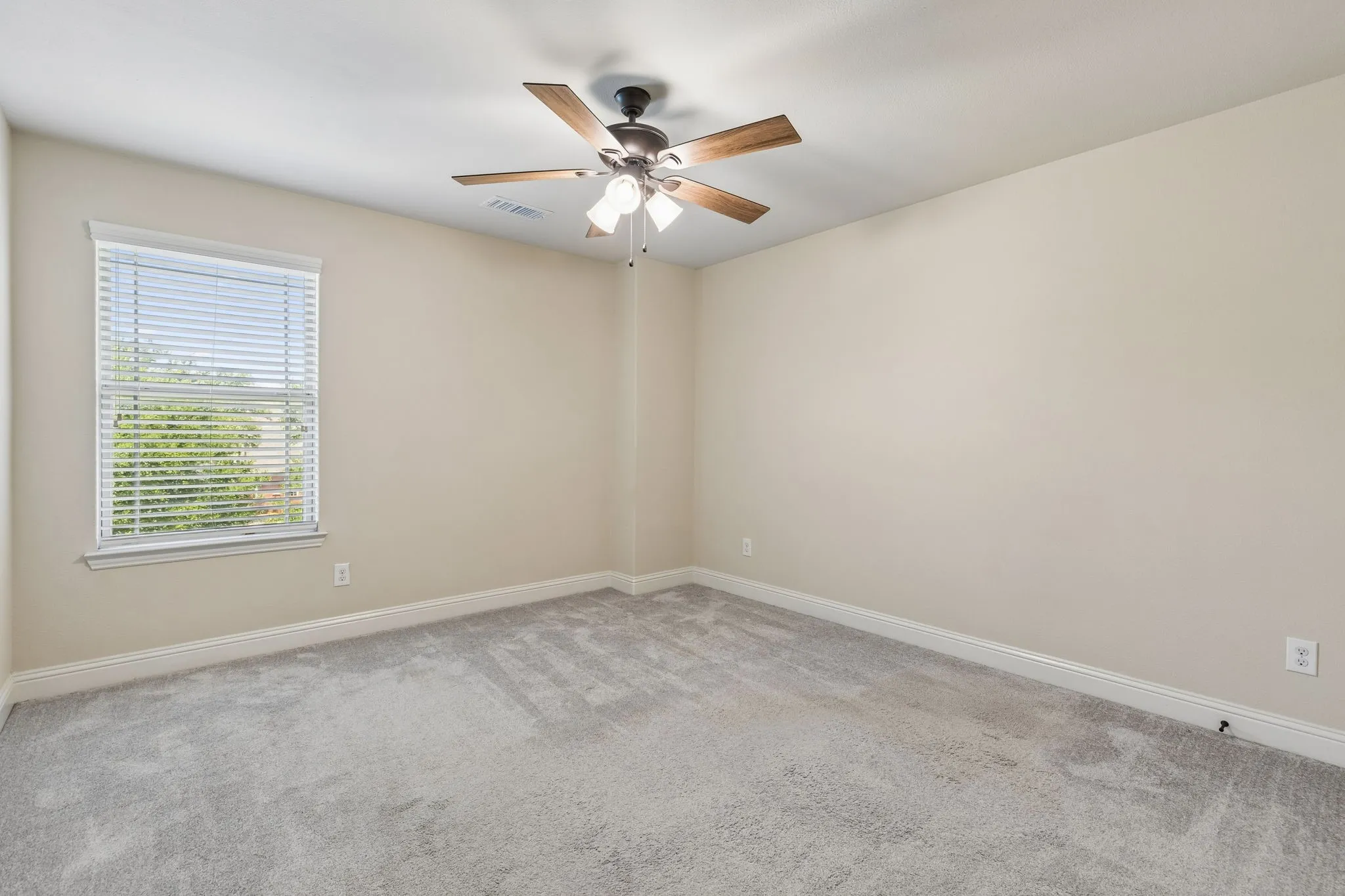 Carpeted bedroom featuring a ceiling fan with light fixture, window with blinds, and neutral wall paint