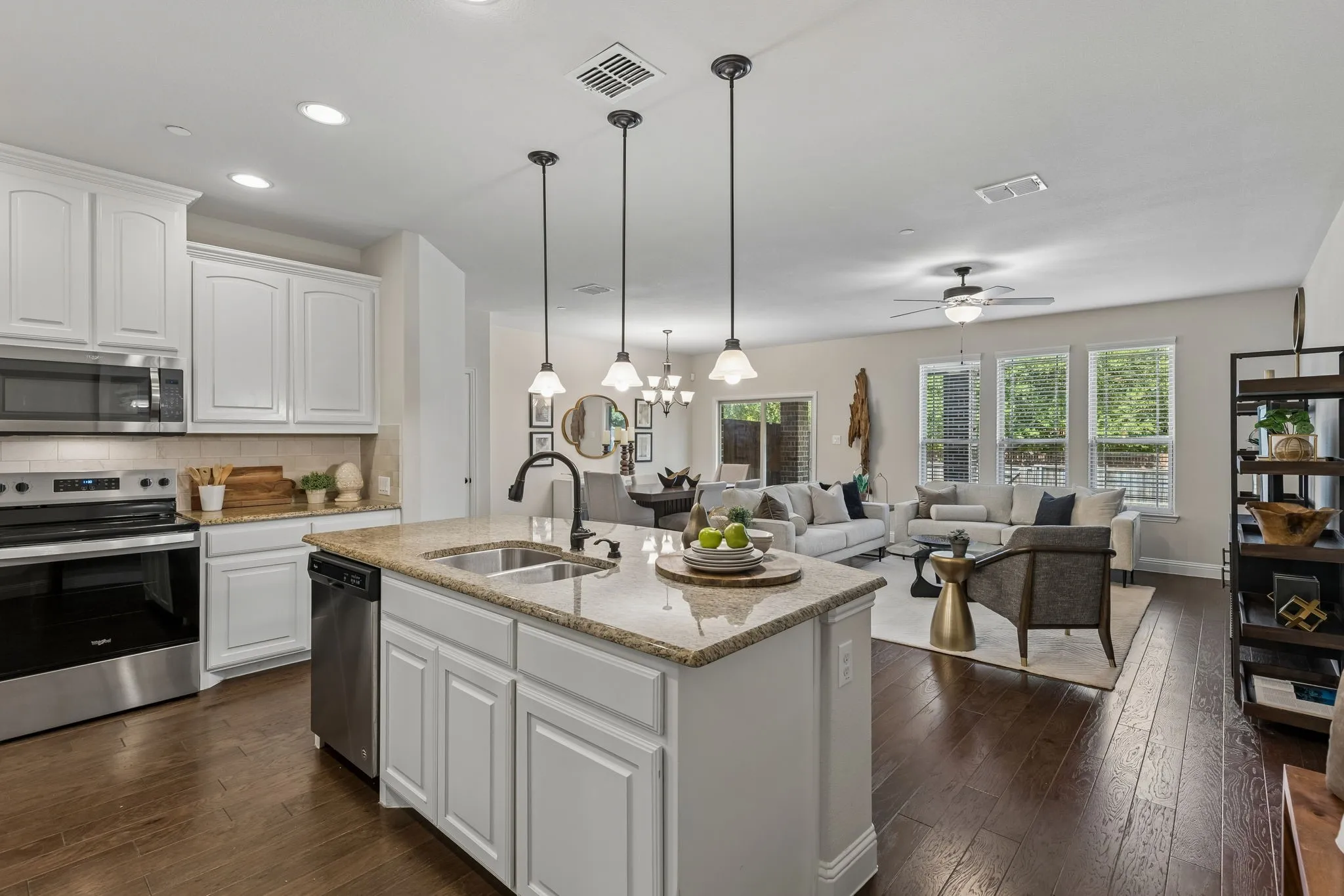 Open-concept living area featuring a kitchen island with sink, white cabinetry, stainless steel appliances, and wood-finish flooring