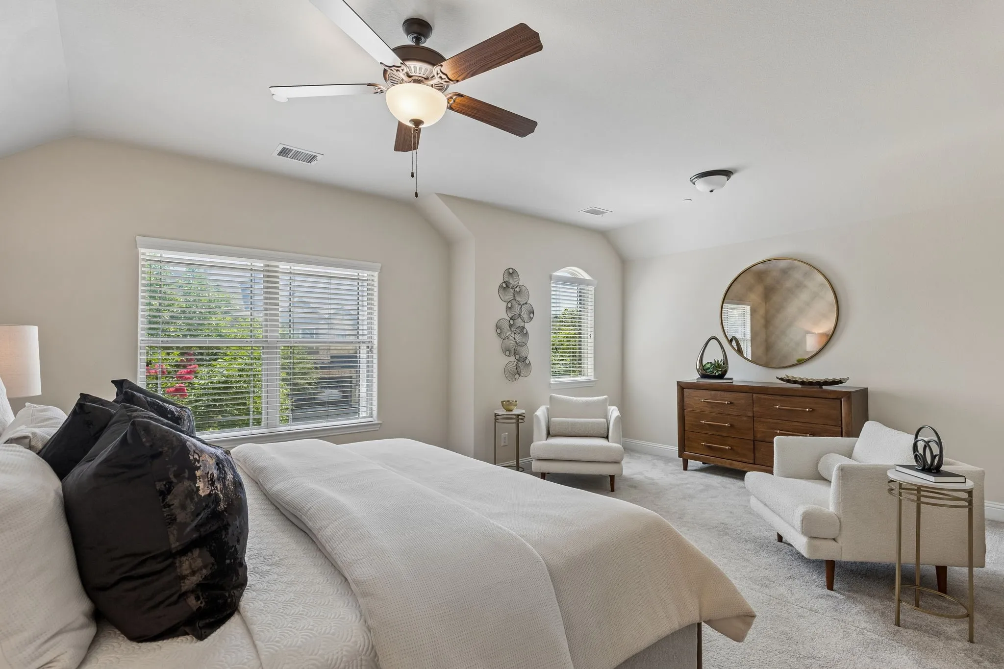 Spacious room featuring vaulted ceilings, a ceiling fan with integrated lighting, a large window with blinds, and light-toned carpet flooring
