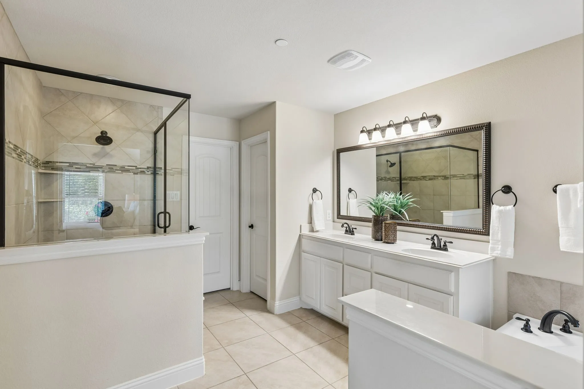 Bathroom featuring a spacious walk-in shower with tile surround, a double vanity with white cabinetry, a large framed mirror, and a built-in tub with dark fixtures