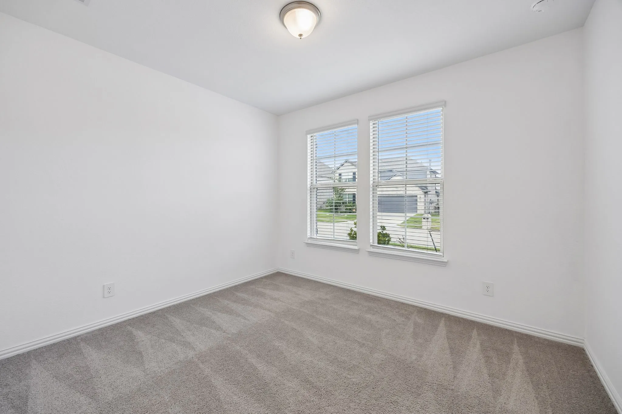 1st floor guest bedroom with white walls defining a bright room with dual windows, gray patterned carpet, white trim, and a flush-mount ceiling light