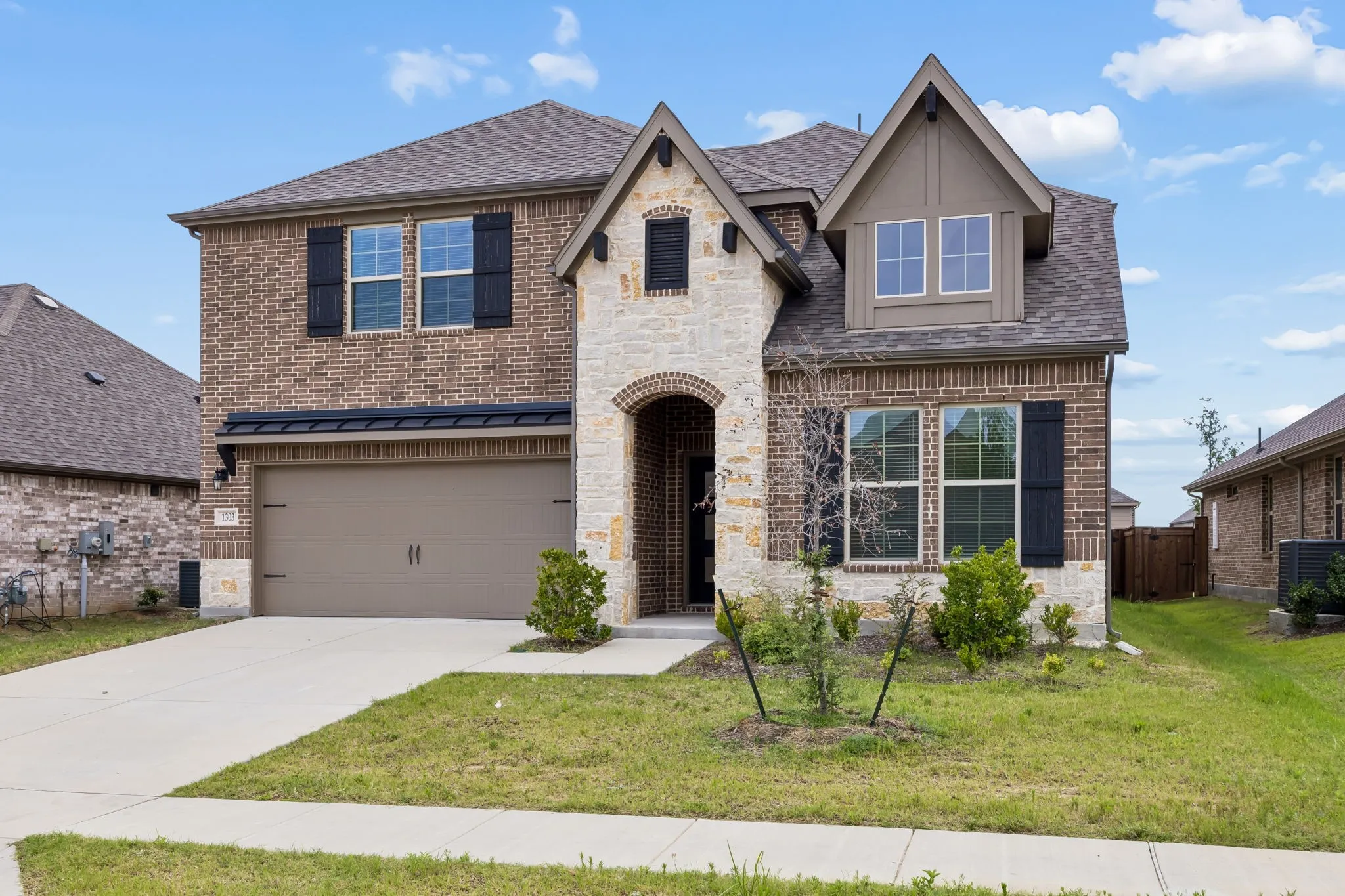 Two-story residence featuring a brick and stone facade, arched entryway, and dark shutters