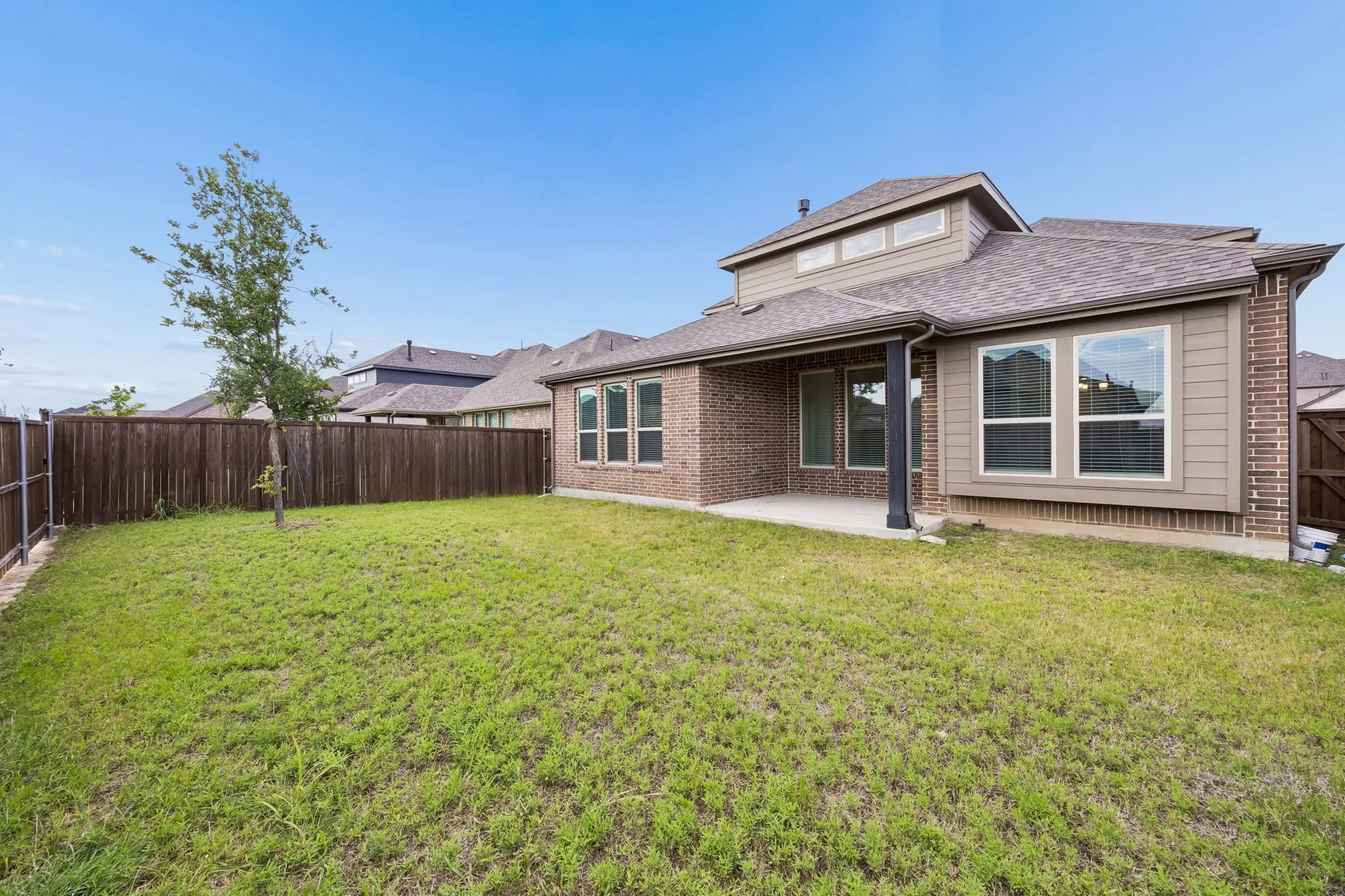Spacious backyard featuring a privacy fence, covered patio, brick exterior, and multiple large windows