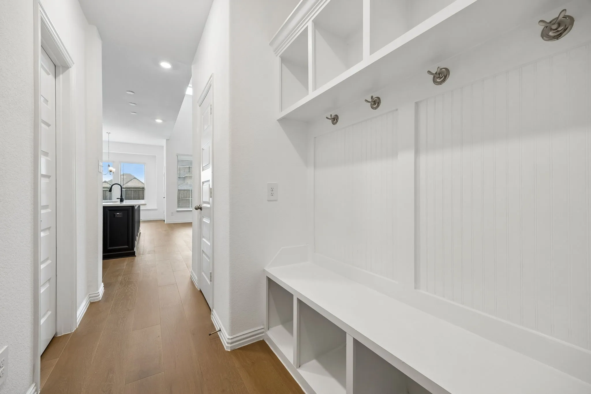 Built-in white storage bench with open shelving, beadboard backing, and metal coat hooks