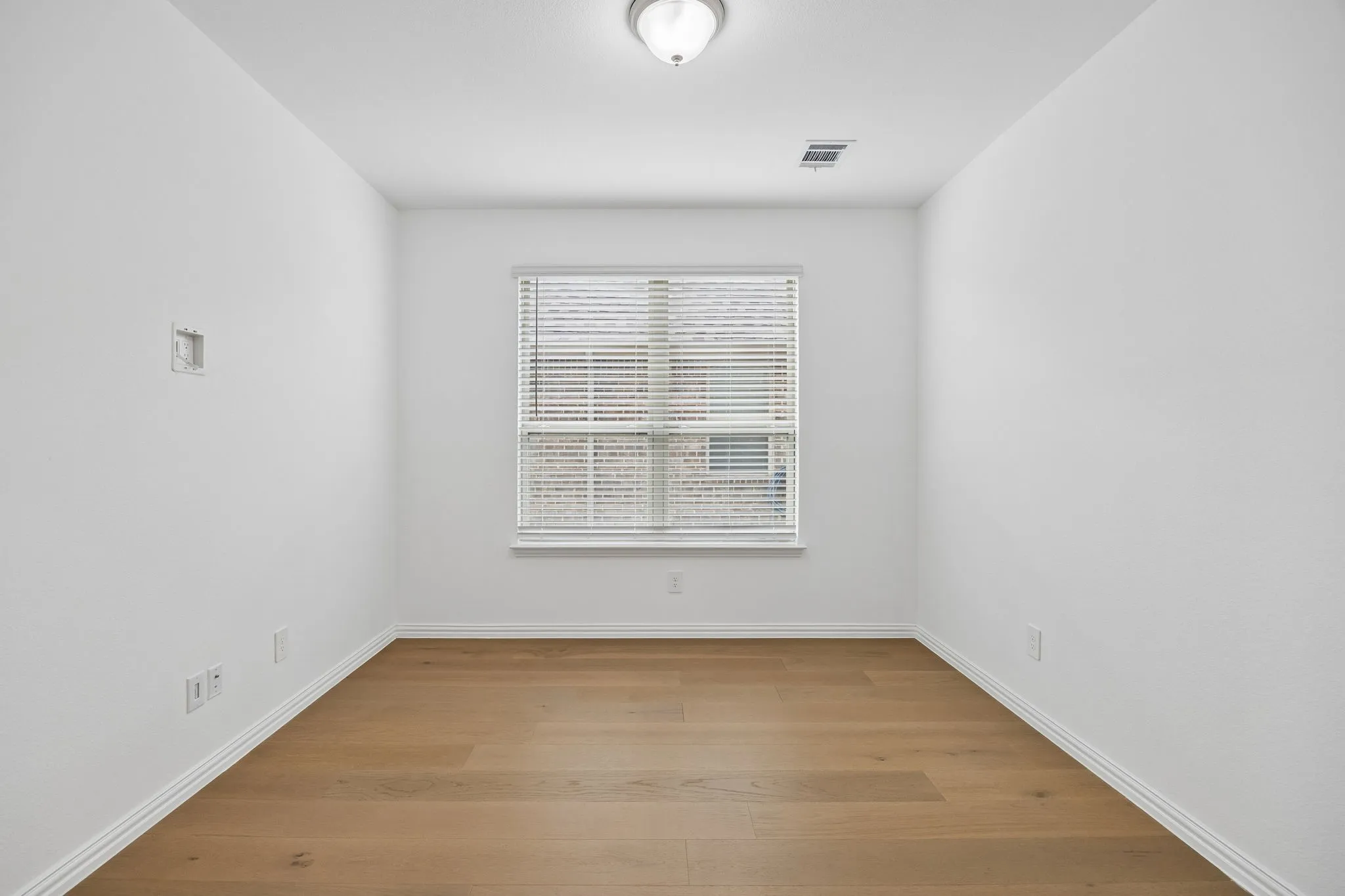 Room featuring light wood-finish flooring, white baseboards, and a single window with blinds