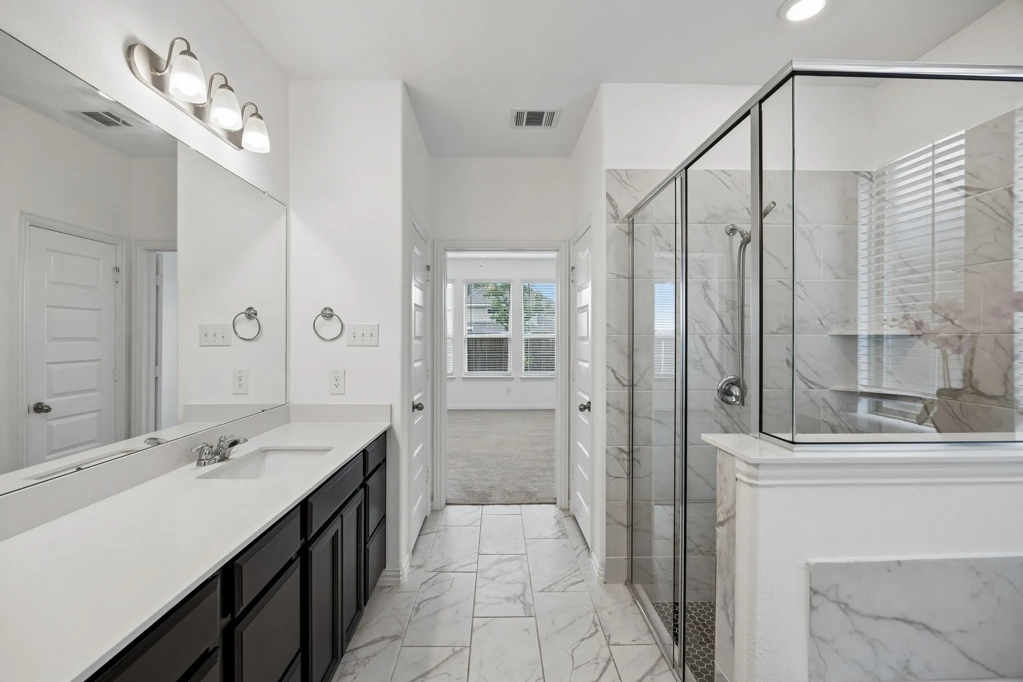 Spacious bathroom featuring a glass-enclosed shower with tile surround, a double vanity with ample counter space, and modern light fixtures