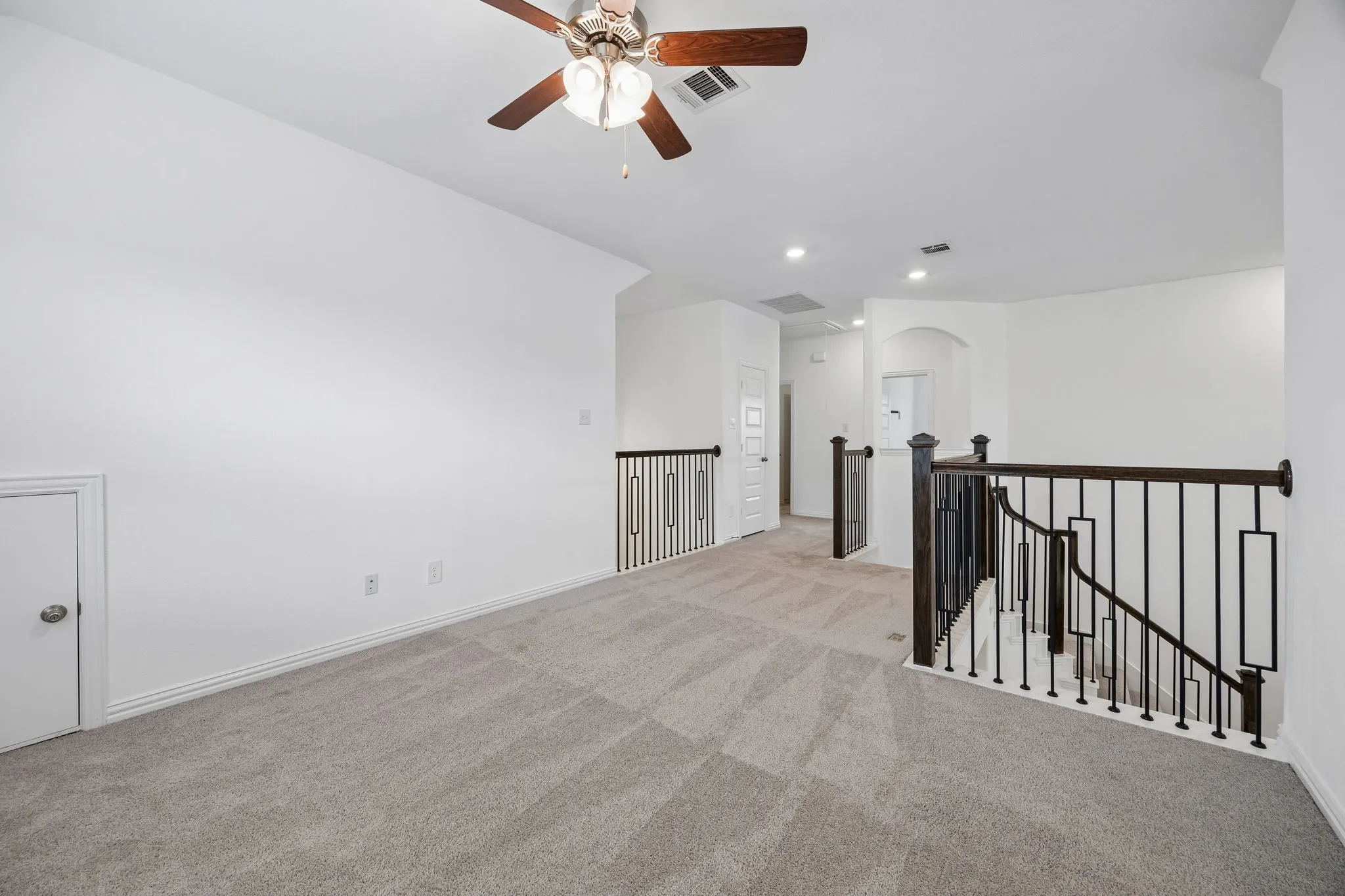 Spacious carpeted landing featuring a ceiling fan, recessed lighting, white walls, and a contemporary black iron stair railing