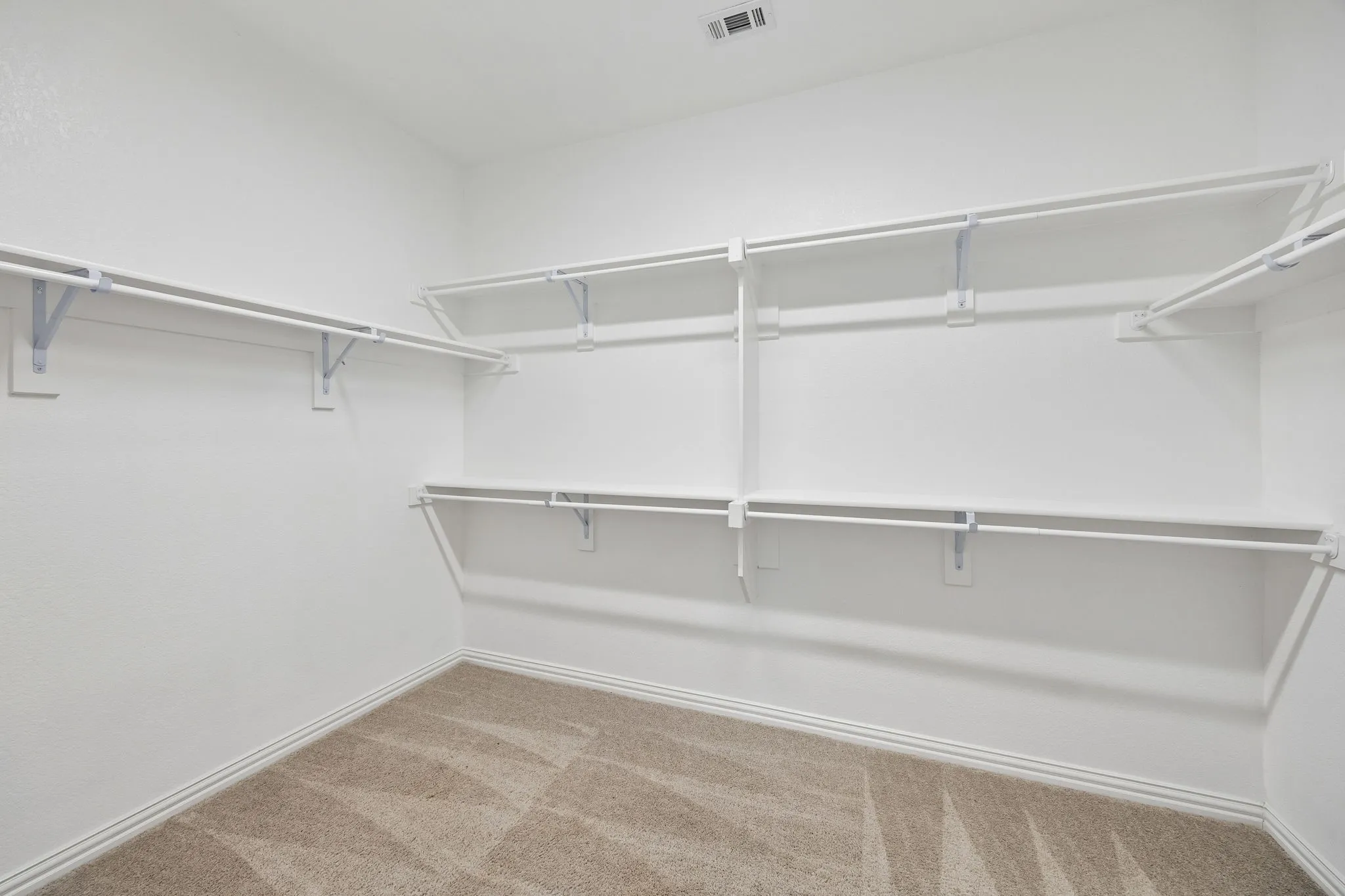 Walk-in closet featuring white wire shelving, multiple hanging rods, and light brown patterned carpet flooring