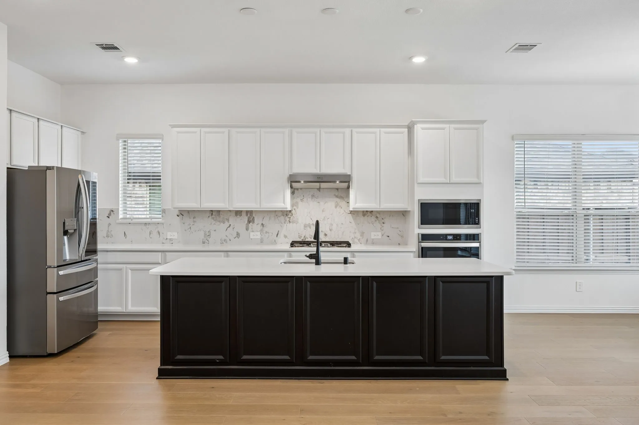 Kitchen featuring a dark-toned island with a white countertop, stainless steel appliances, white cabinetry, a light-toned backsplash, and wood-finish flooring