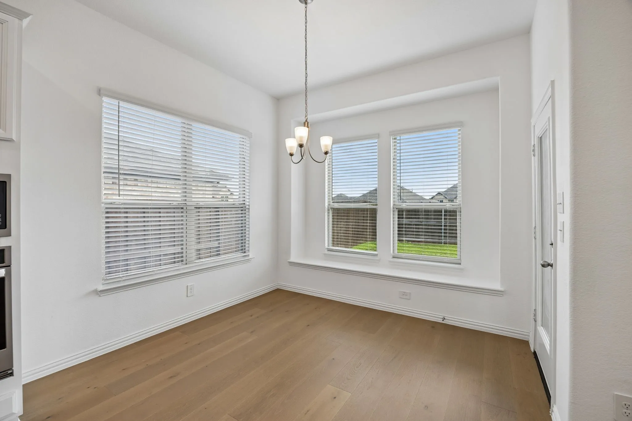 Bright dining area with wood-finish flooring, a contemporary chandelier, multiple windows with blinds, a window seat, and a paneled door