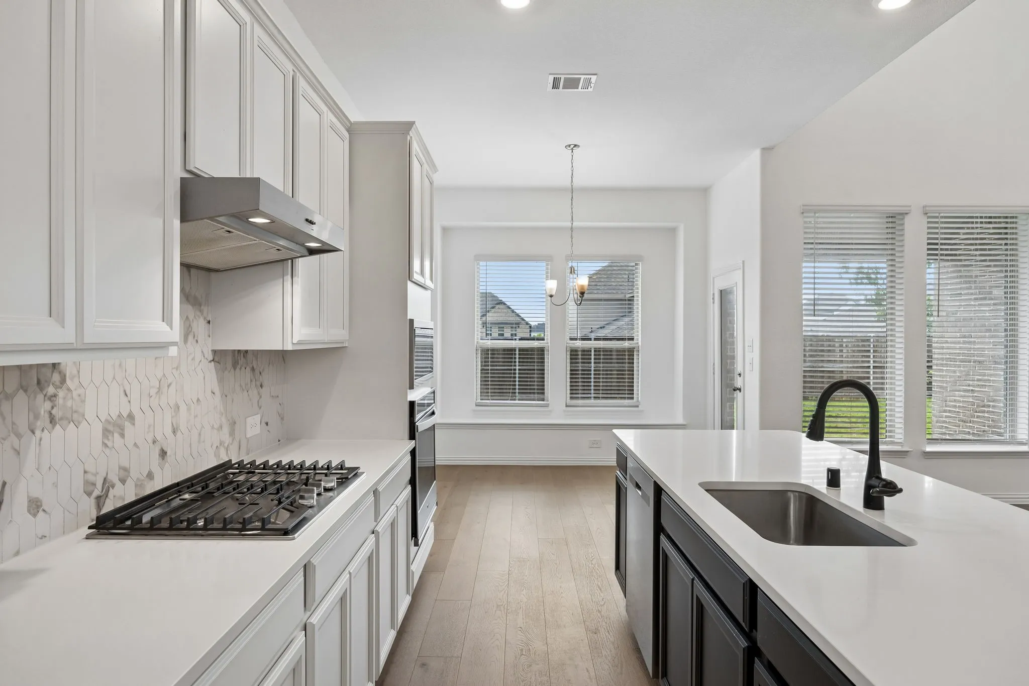 Modern kitchen featuring white shaker-style cabinetry, a built-in gas range with a stainless steel vent hood, and a geometric tile backsplash