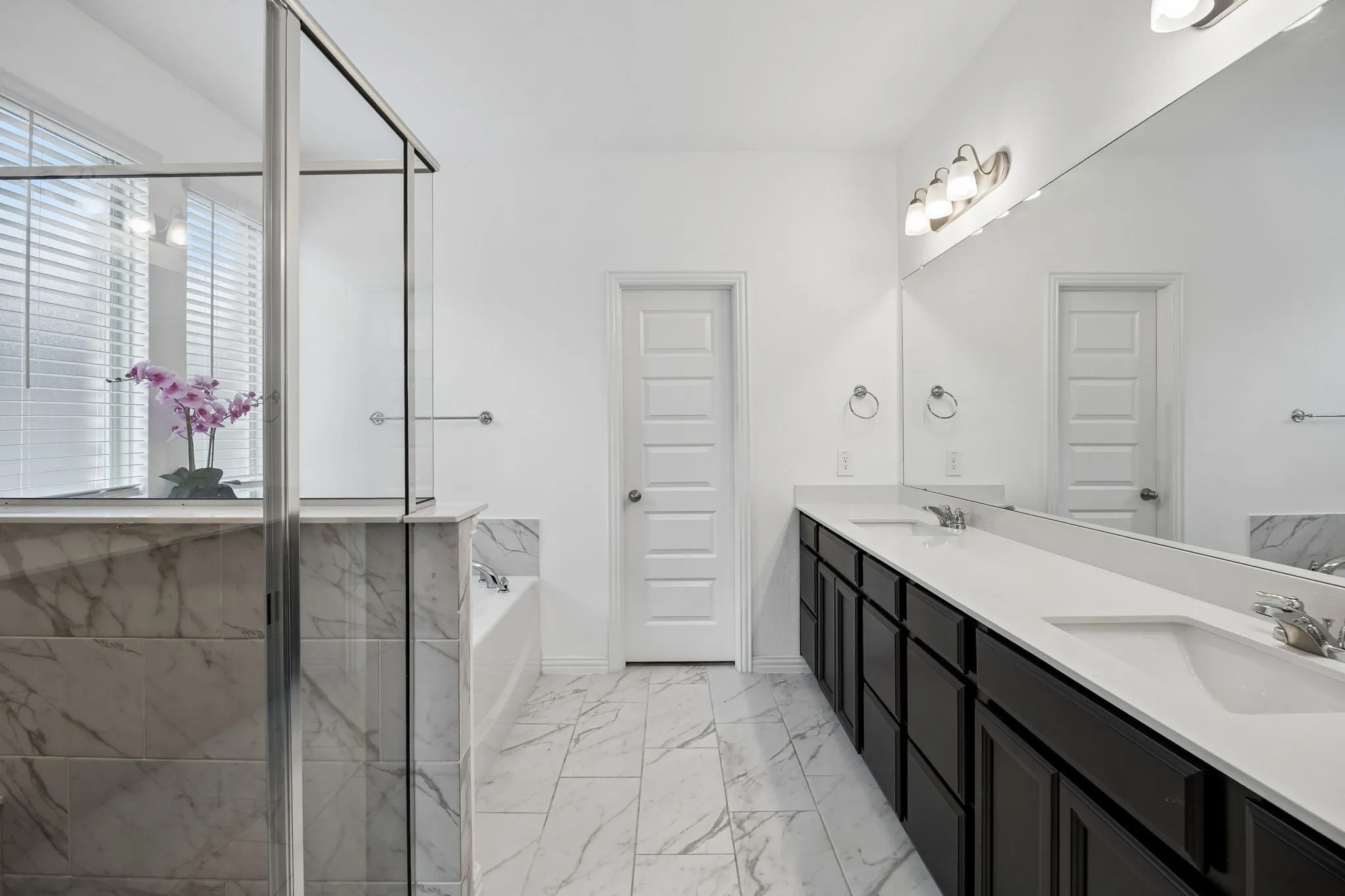 Spacious bathroom featuring a glass-enclosed shower, a separate soaking tub, and a long double vanity with integrated sinks