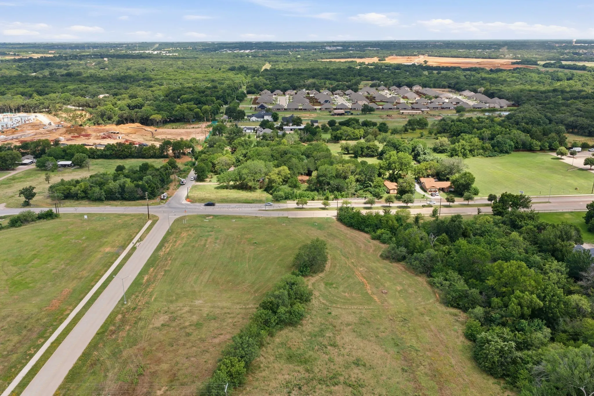 Expansive green acreage featuring a clear parcel, a paved road, and a cross intersection