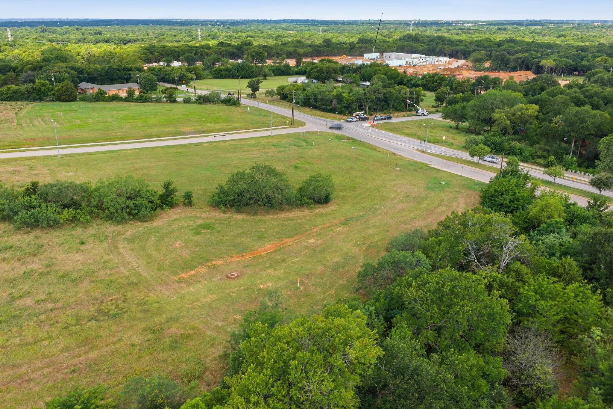 Expansive green space featuring a paved road, mature trees, and visible construction in the distance