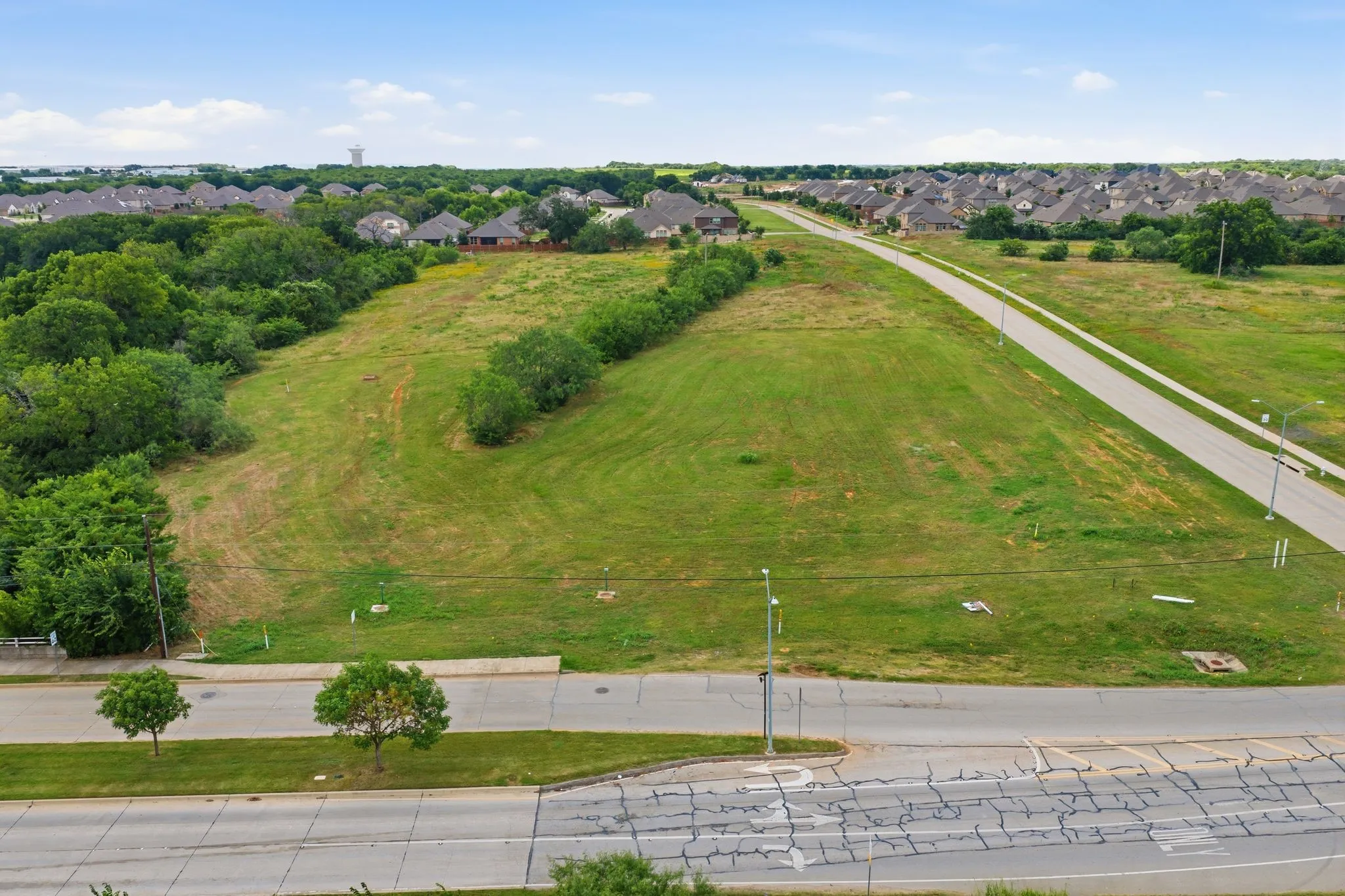 Expansive land parcel featuring a paved road, streetlights, and surrounding greenery