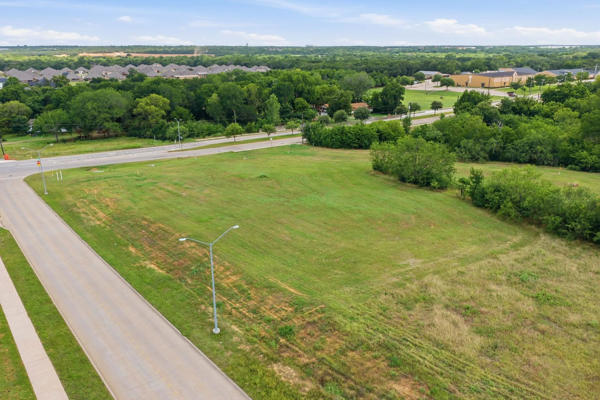 Expansive green lot featuring a paved road, sidewalk, and streetlights