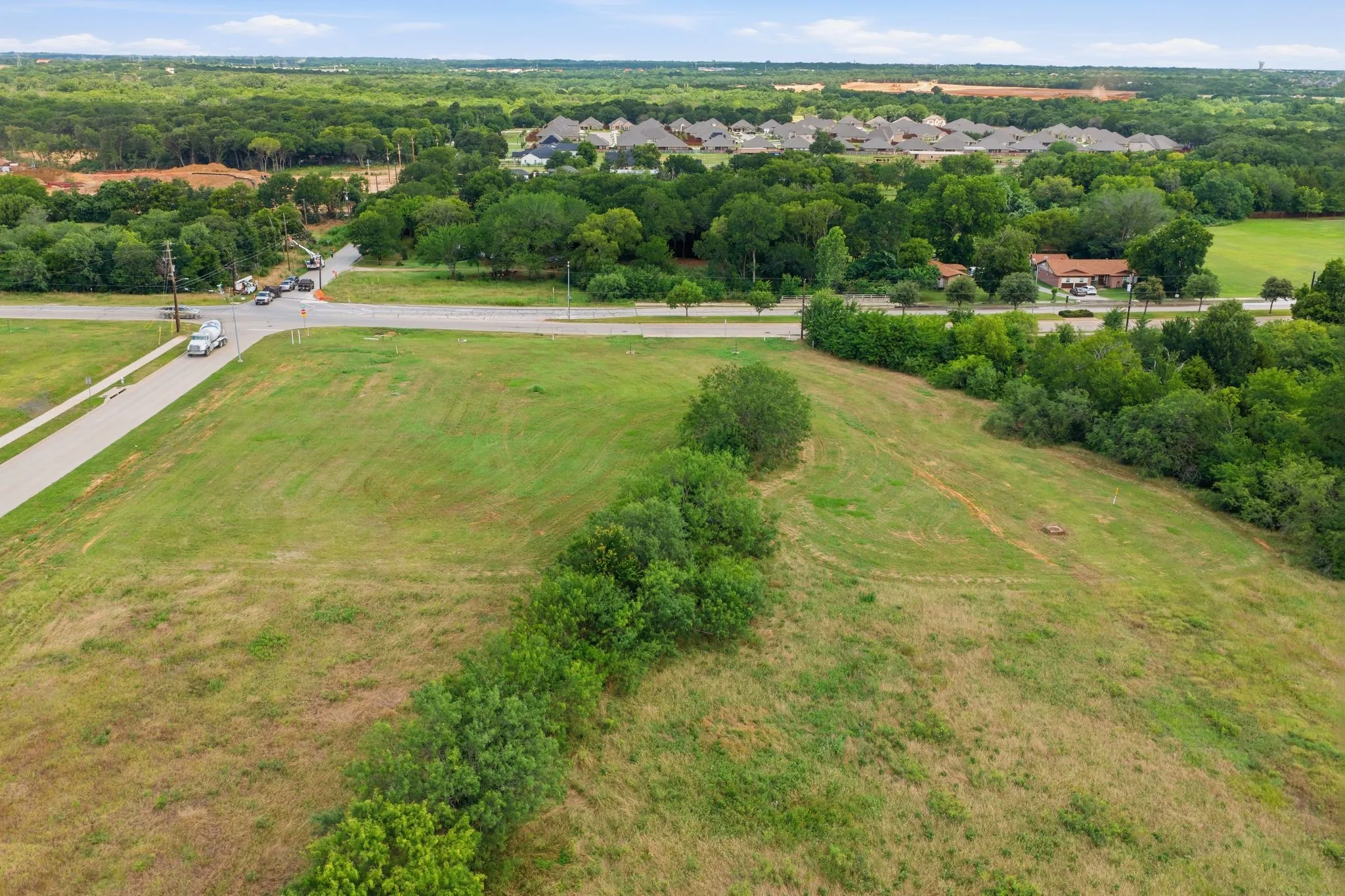 Expansive undeveloped parcel featuring a verdant landscape, mature tree lines, and paved road frontage