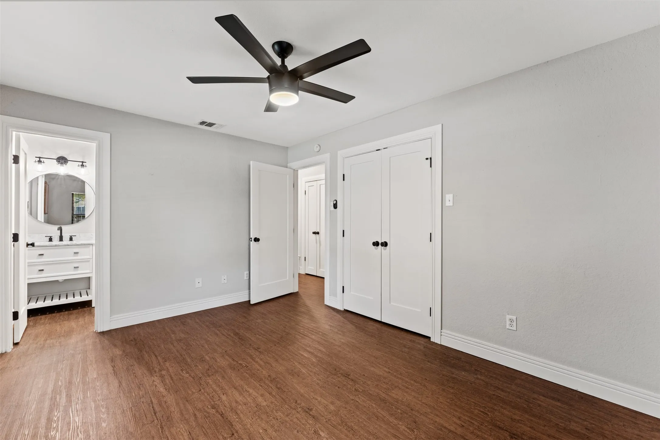 Neutral-toned room featuring wood-finish flooring, a contemporary ceiling fan, and white baseboards