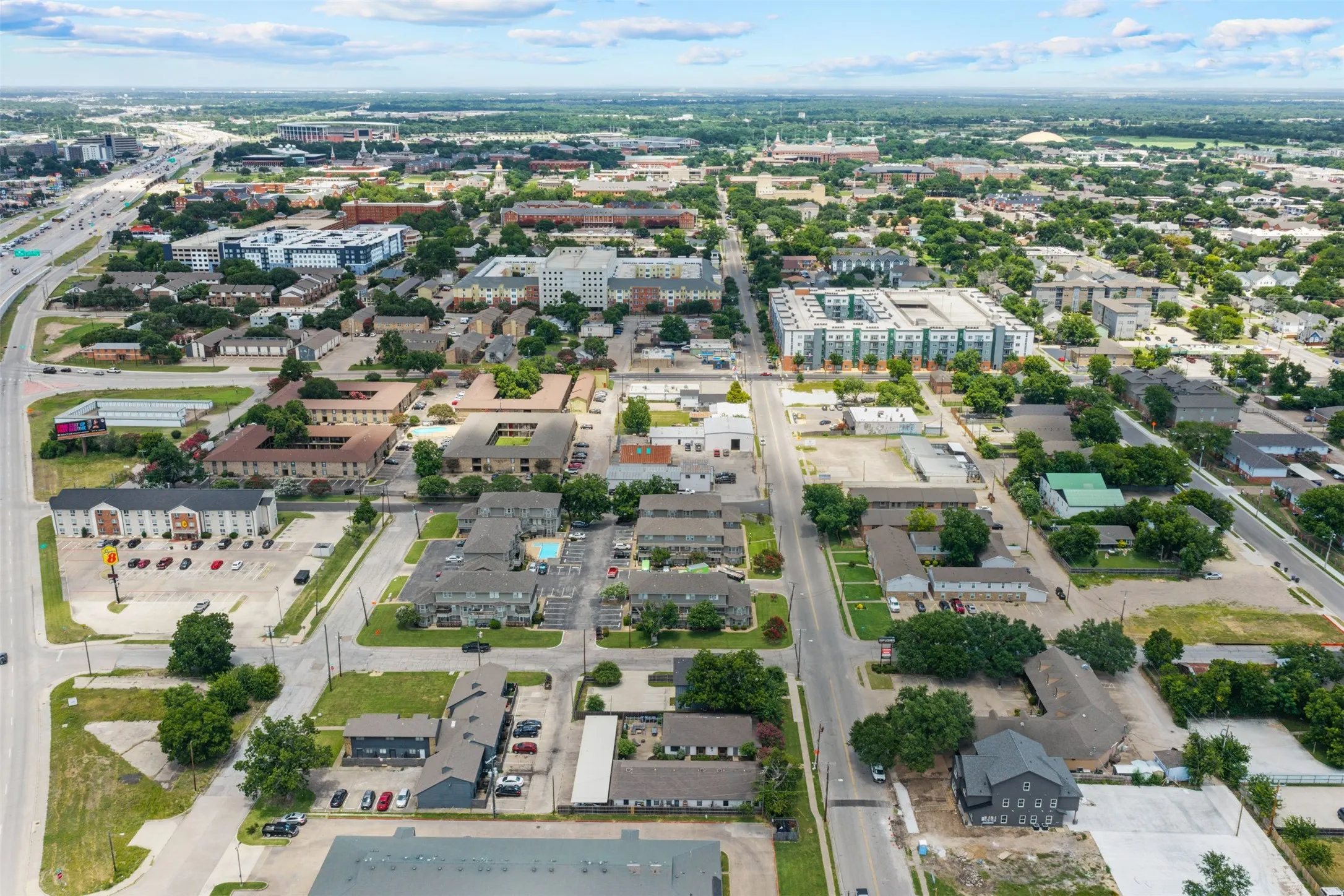 Aerial perspective of a developed urban area featuring diverse multi-story buildings, established tree canopy, and arterial roadways
