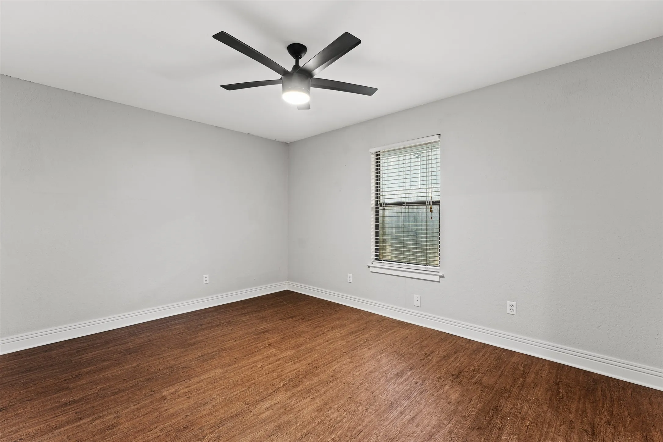 Spacious room featuring wood-finish flooring, light gray walls, and white baseboards