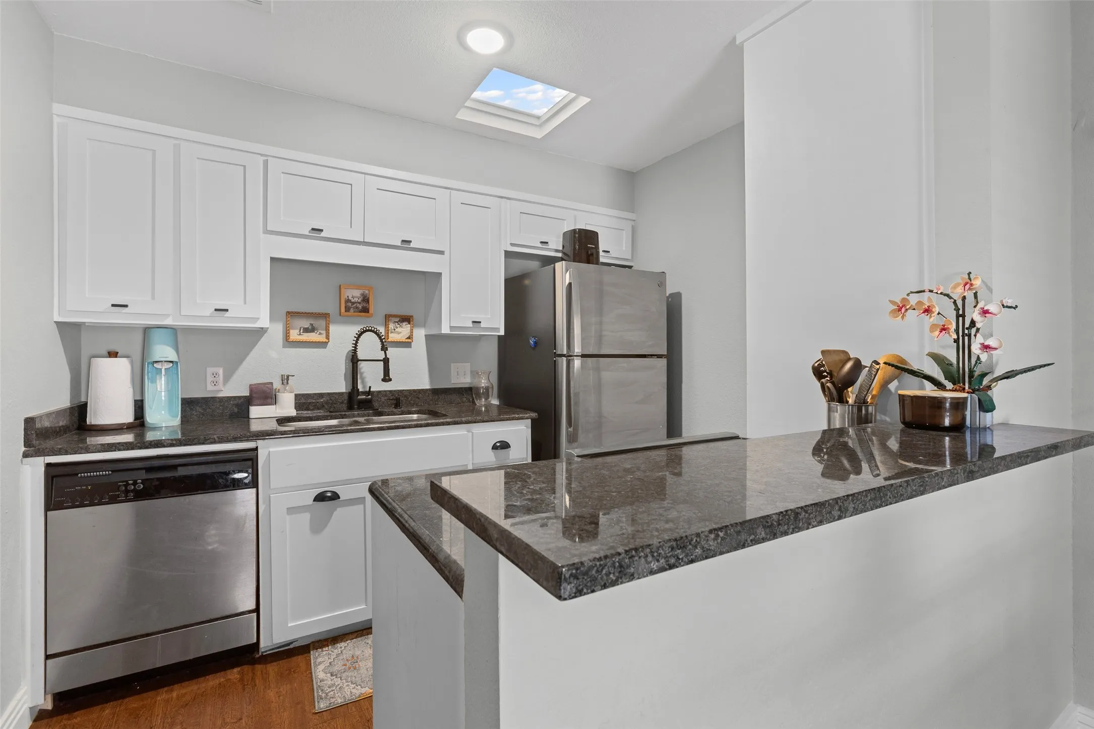 Kitchen featuring white cabinetry, dark granite countertops, stainless steel appliances, a bar-height counter, and a skylight