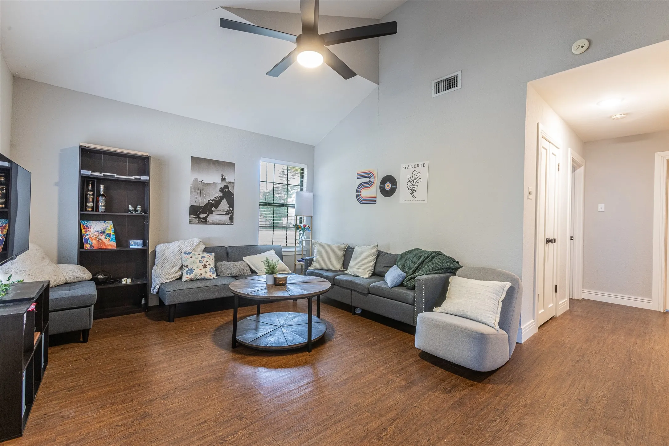 Living space featuring a vaulted ceiling with a ceiling fan, wood-finish flooring, a double window with blinds, and white baseboards