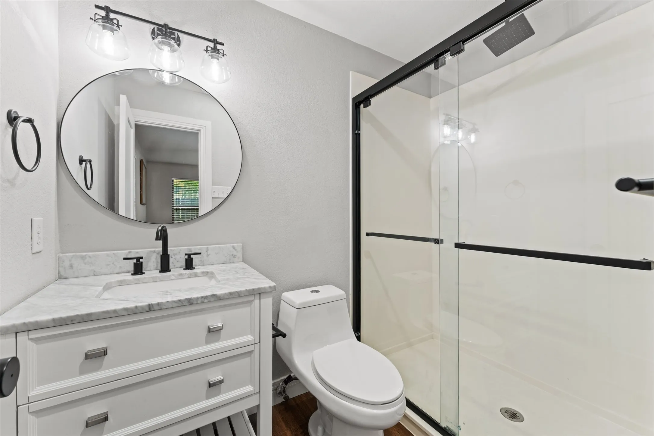 Bathroom featuring a white vanity with a light-toned countertop, a contemporary round mirror, and a matte black three-light fixture