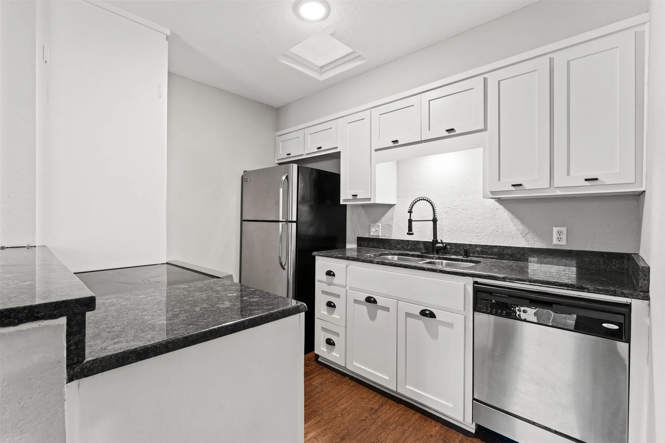 Kitchen featuring white cabinetry, dark granite countertops, stainless steel appliances, and wood-finish flooring