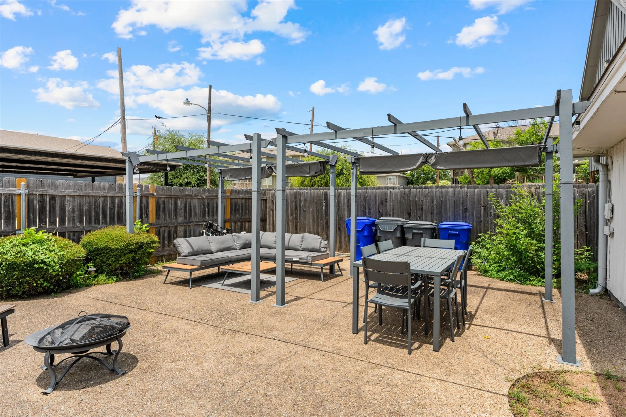 Expansive concrete patio featuring a modern metal pergola with retractable sunshades, offering dedicated outdoor dining and lounging areas