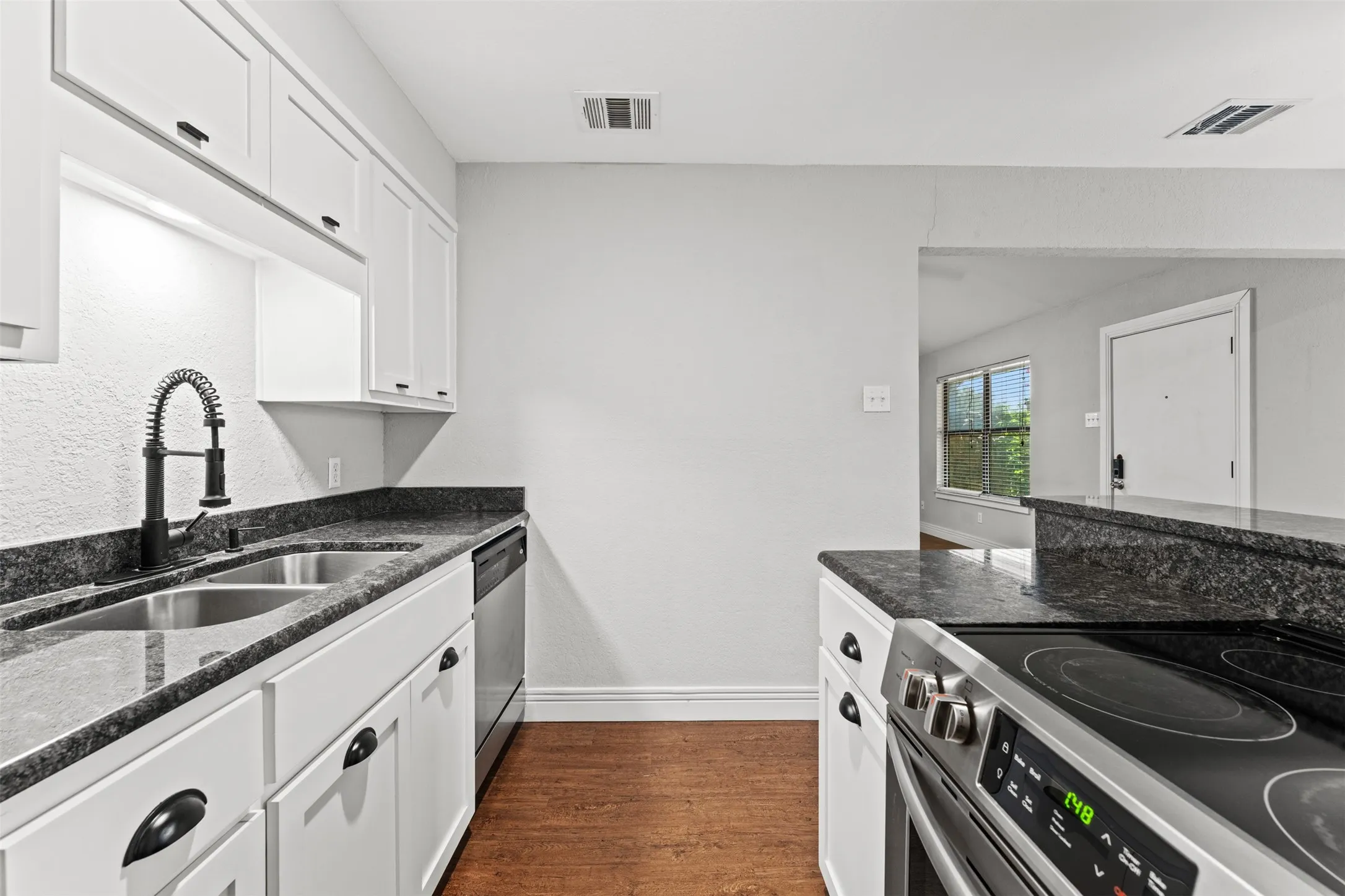 Kitchen featuring white cabinetry, dark stone countertops, stainless steel appliances, and wood-finish flooring