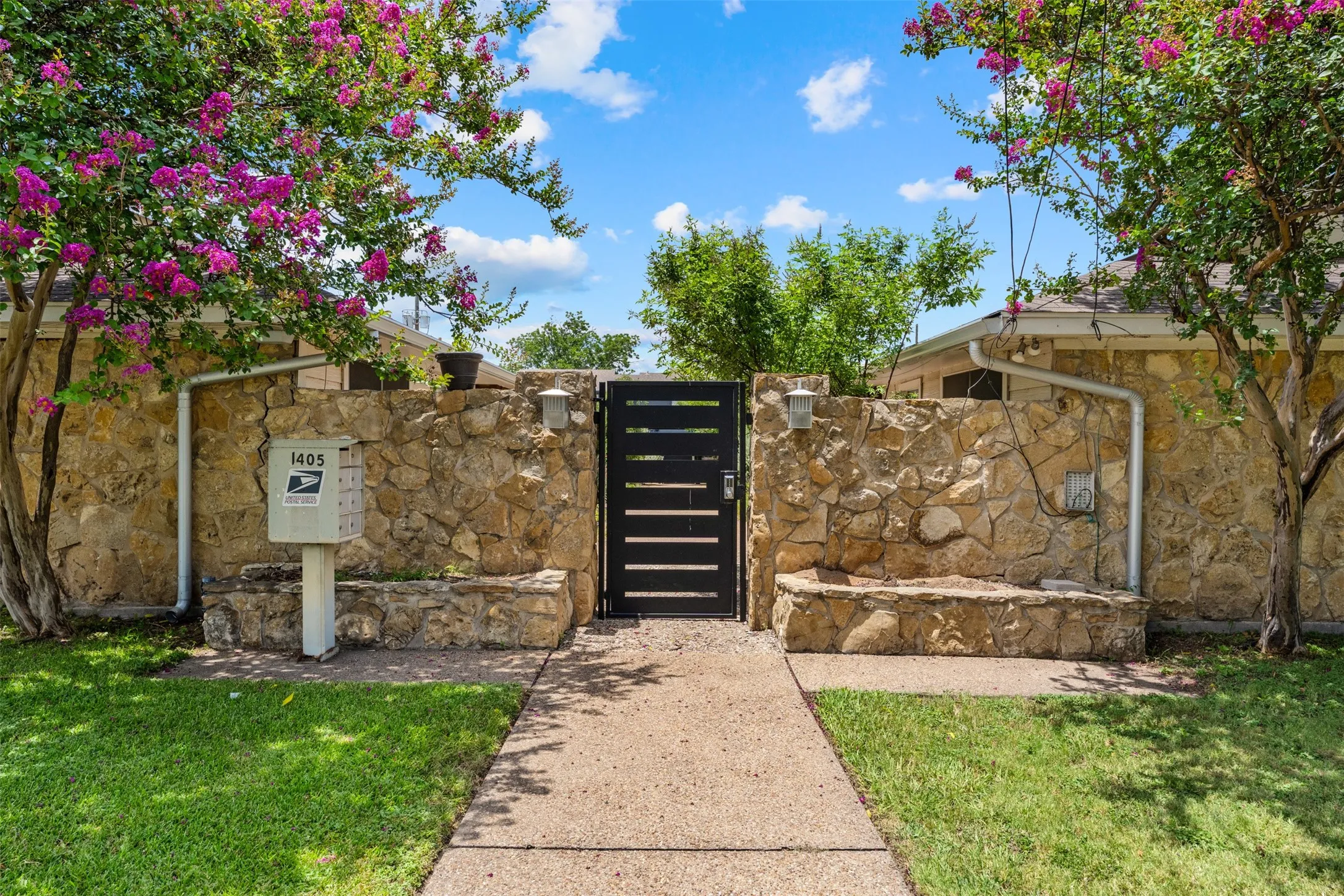 Stone privacy wall with integrated stone bench seating, a black slatted gate, and a concrete pathway