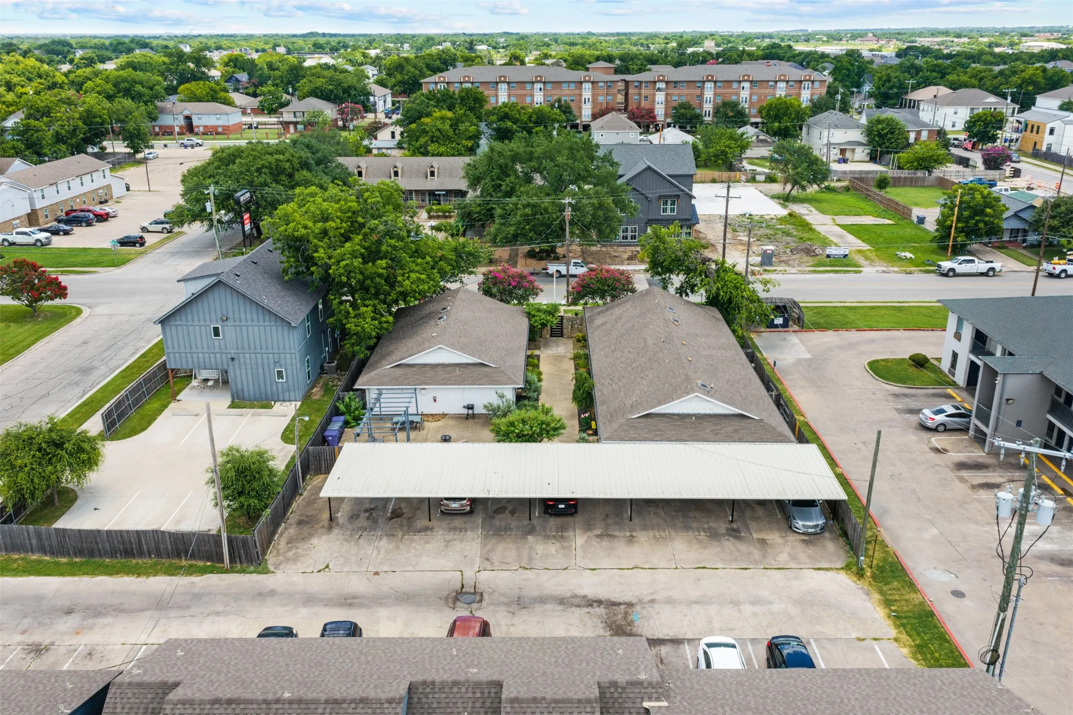 Aerial perspective showcasing multiple properties, including a multi-story building with light blue siding, a single-story building with a light-colored exterior, and a large carport structure