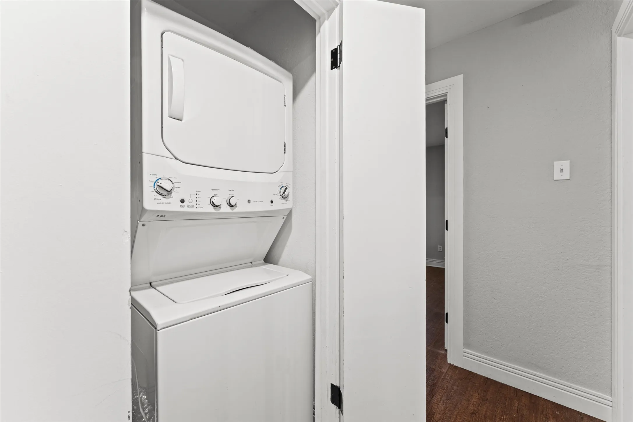 Laundry closet featuring a white stacked washer and dryer, painted white walls, and wood-finish flooring