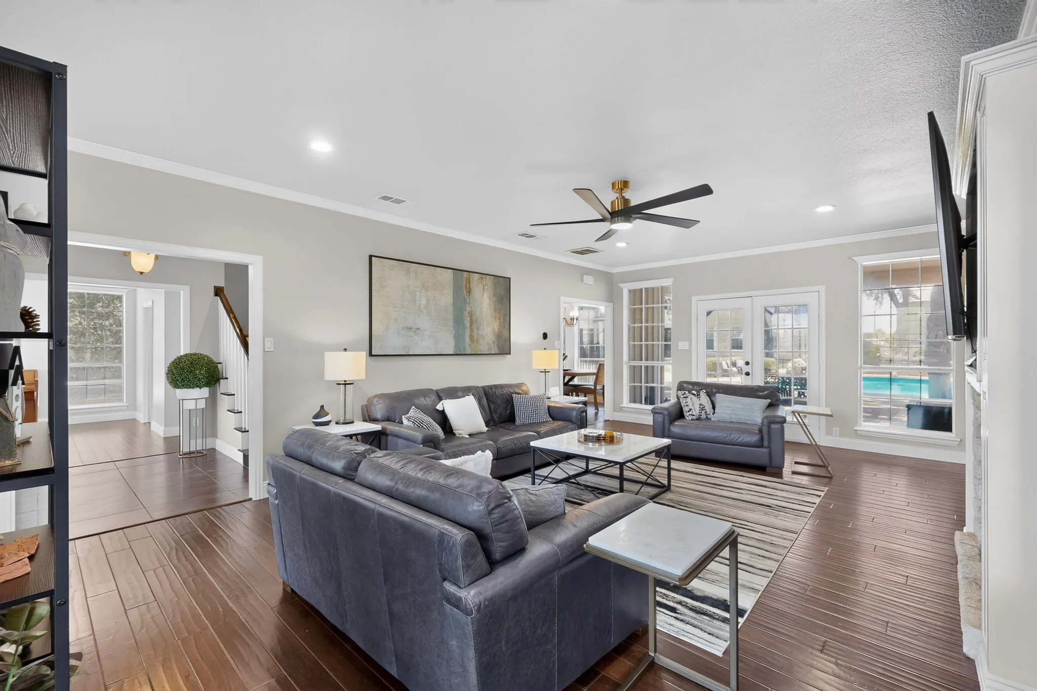 Spacious living area featuring rich wood-finish flooring, a contemporary ceiling fan, recessed lighting, and crown molding