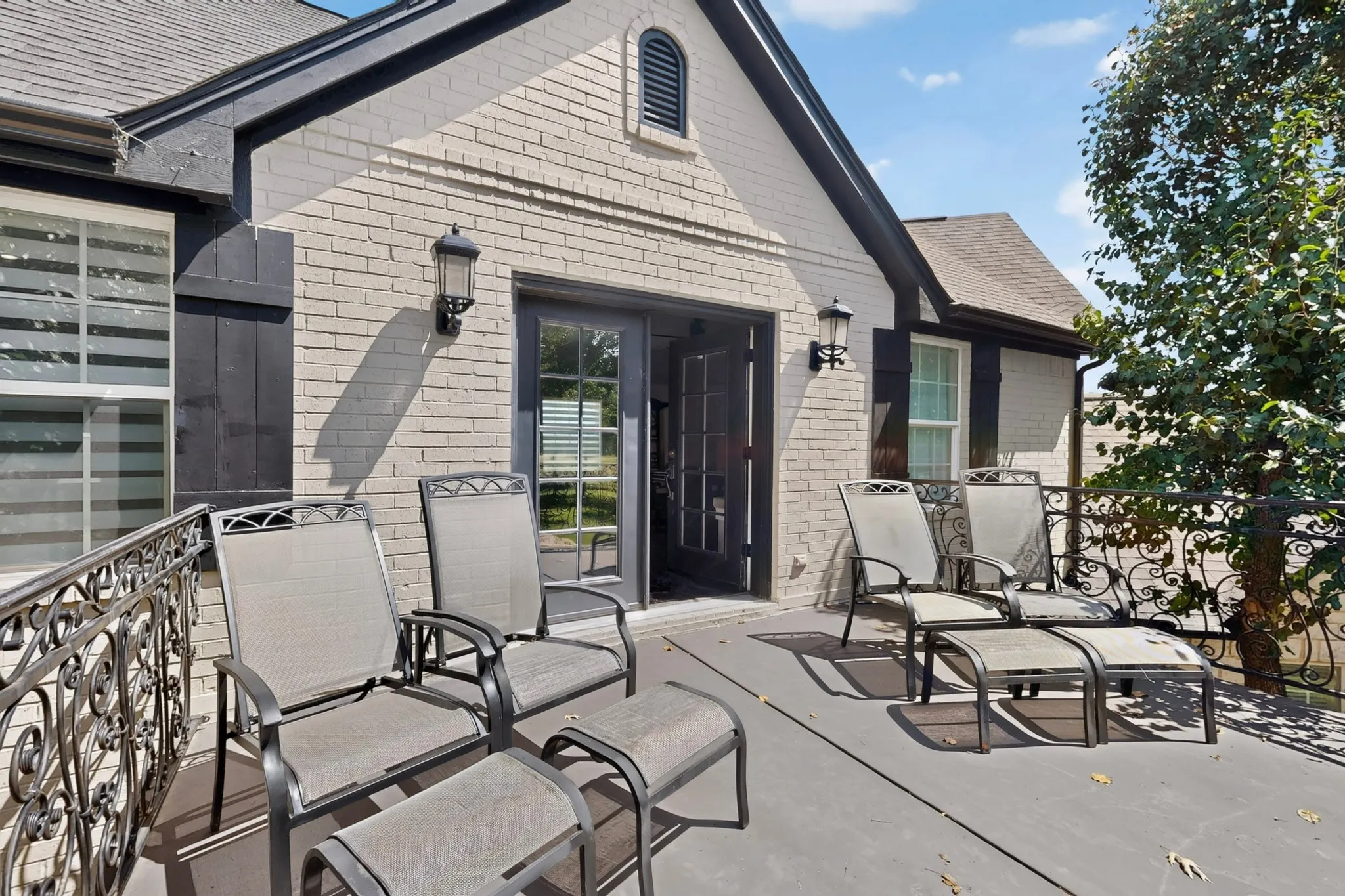 Spacious outdoor deck featuring a dark gray surface, ornate wrought iron railing, and brick exterior