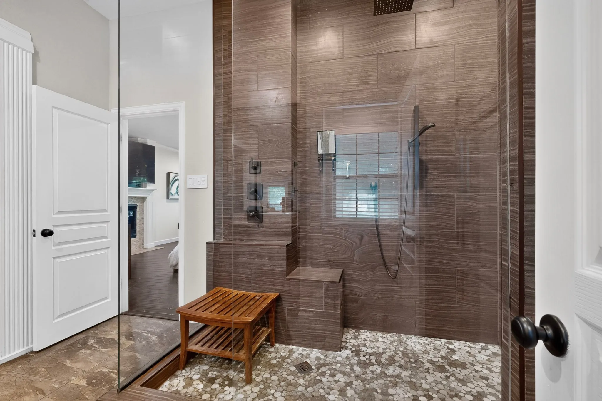 Glass-enclosed shower with wood-finish tile walls, pebble floor, built-in bench, and rain shower head