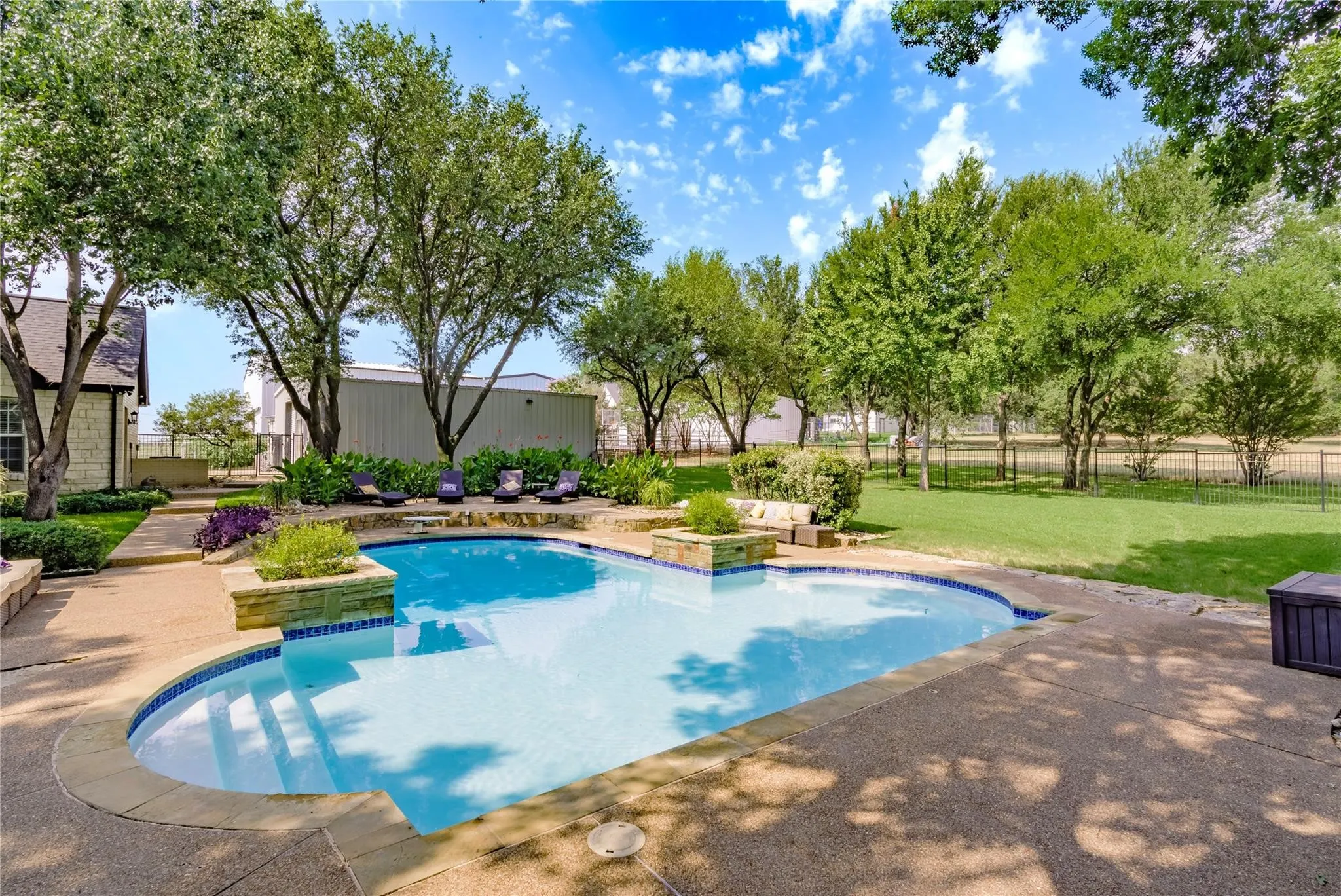 Outdoor pool featuring a curved design with integrated steps, surrounded by stamped concrete decking and stone-clad planters